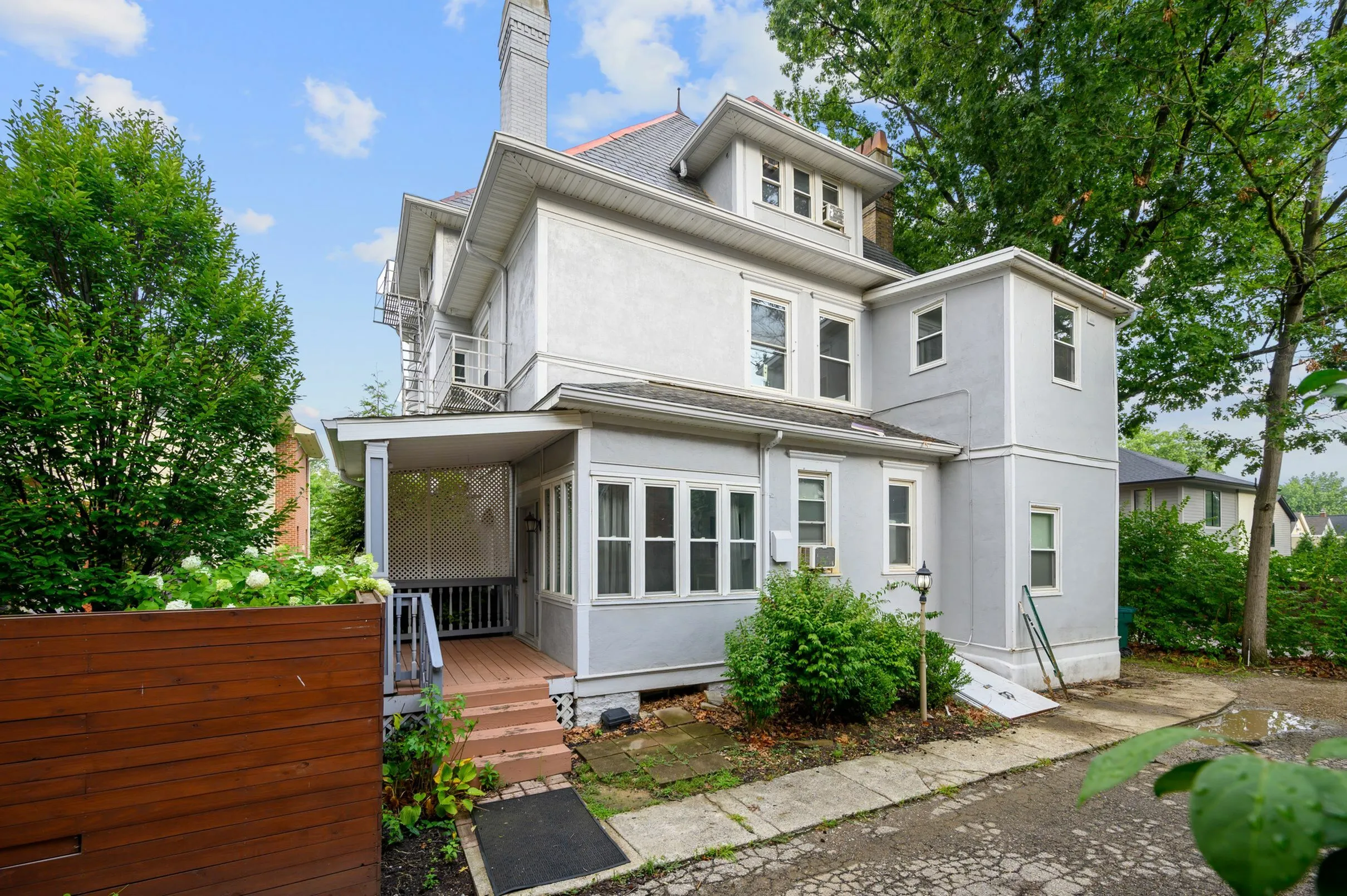 Charming multi-story home with a spacious veranda and lush greenery, perfect for serene living.