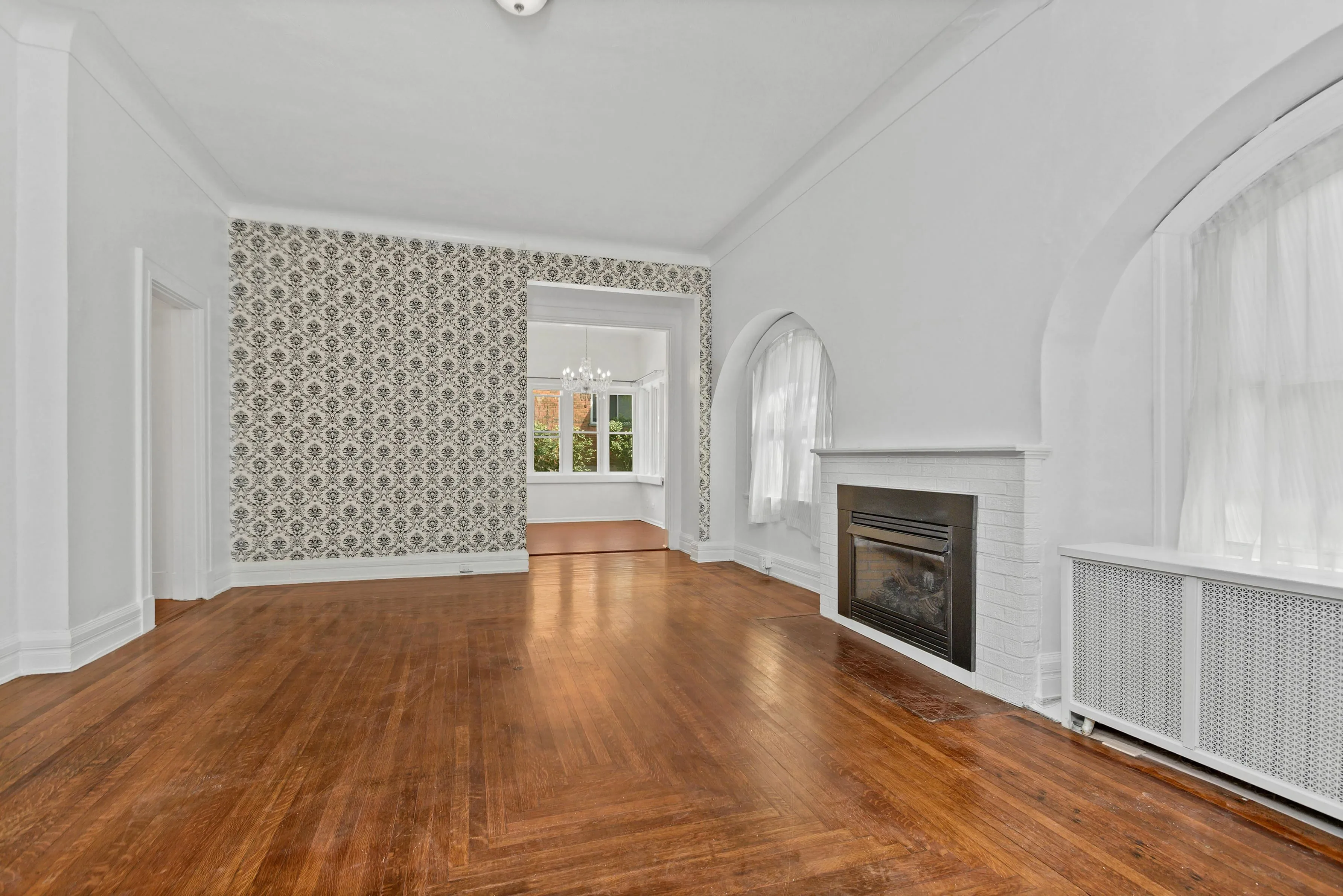 Charming living room with elegant hardwood floors, a cozy fireplace, and a stylish arched window.