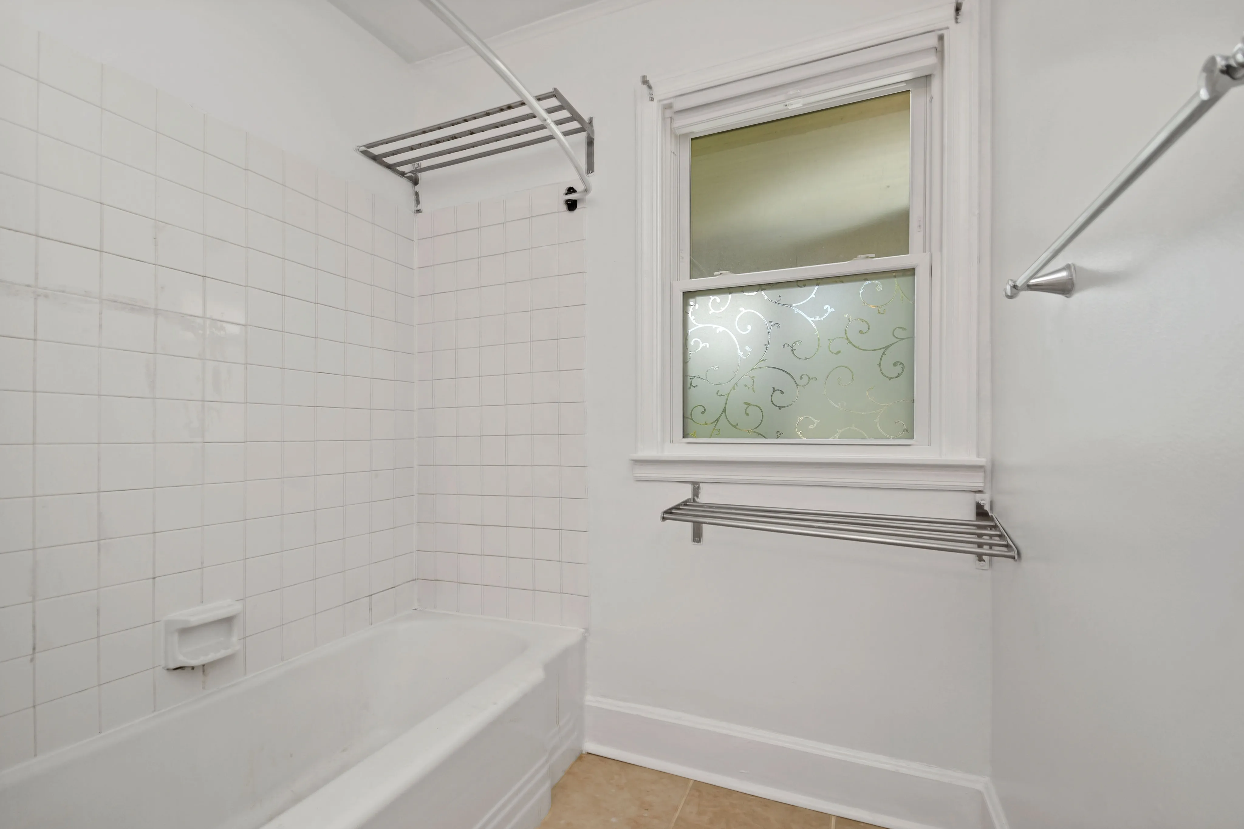 Bright and modern bathroom featuring a sleek bathtub with white tiles and frosted patterned window for privacy.