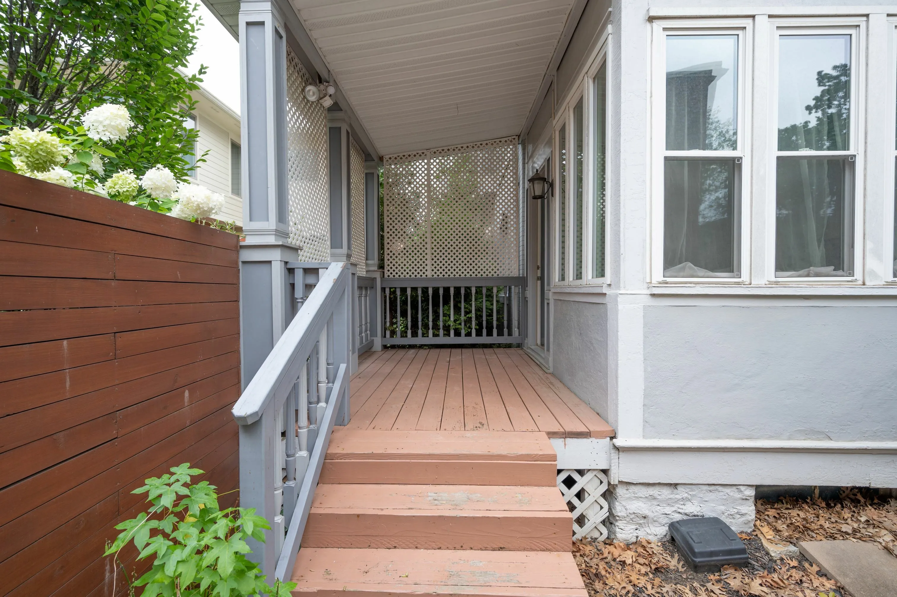 Charming front porch with elegant wooden steps and decorative lattice, offering a cozy entryway surrounded by lush greenery and vibrant flowers.