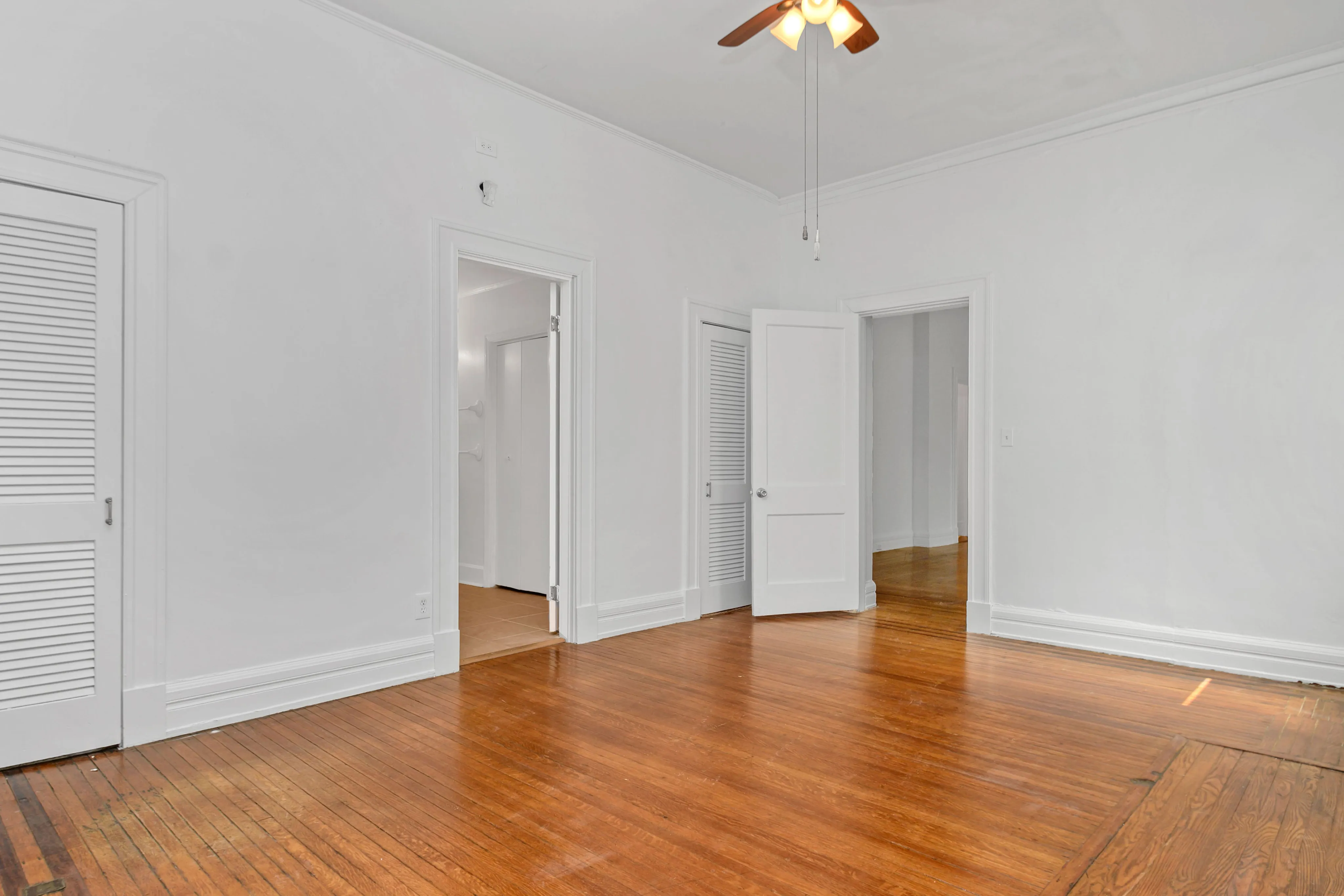 Bright room with warm wooden floors, white doors, and a ceiling fan, ideal for a cozy living space.