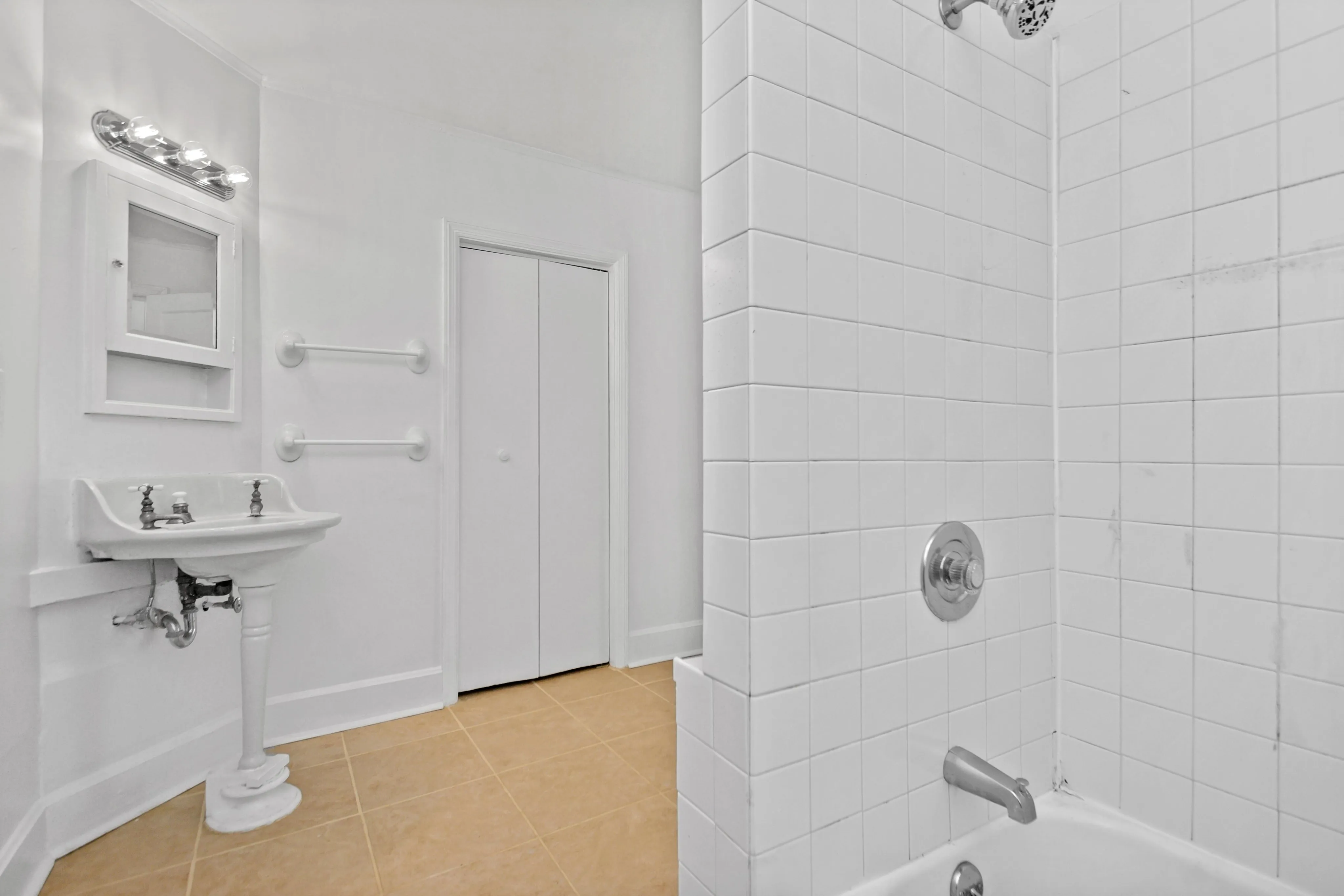 Bright, modern bathroom showcasing a classic white tile design with a pedestal sink and bathtub.