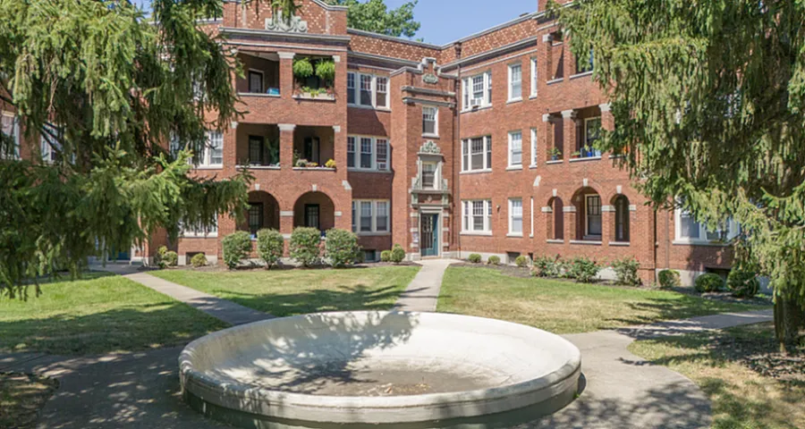 Charming brick apartment building with lush greenery, featuring a serene central courtyard and welcoming pathways.