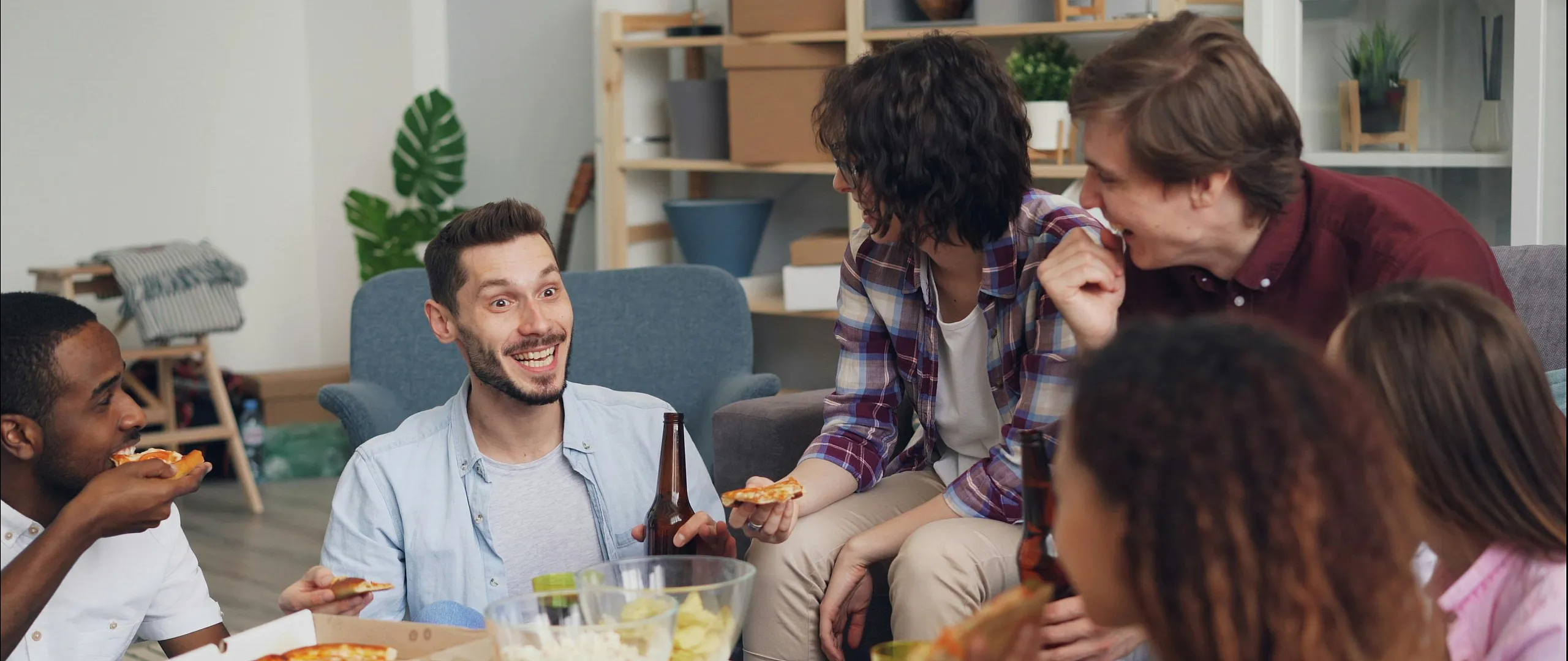 Vibrant living room scene with friends enjoying pizza and drinks, highlighting a cozy and inviting apartment atmosphere.