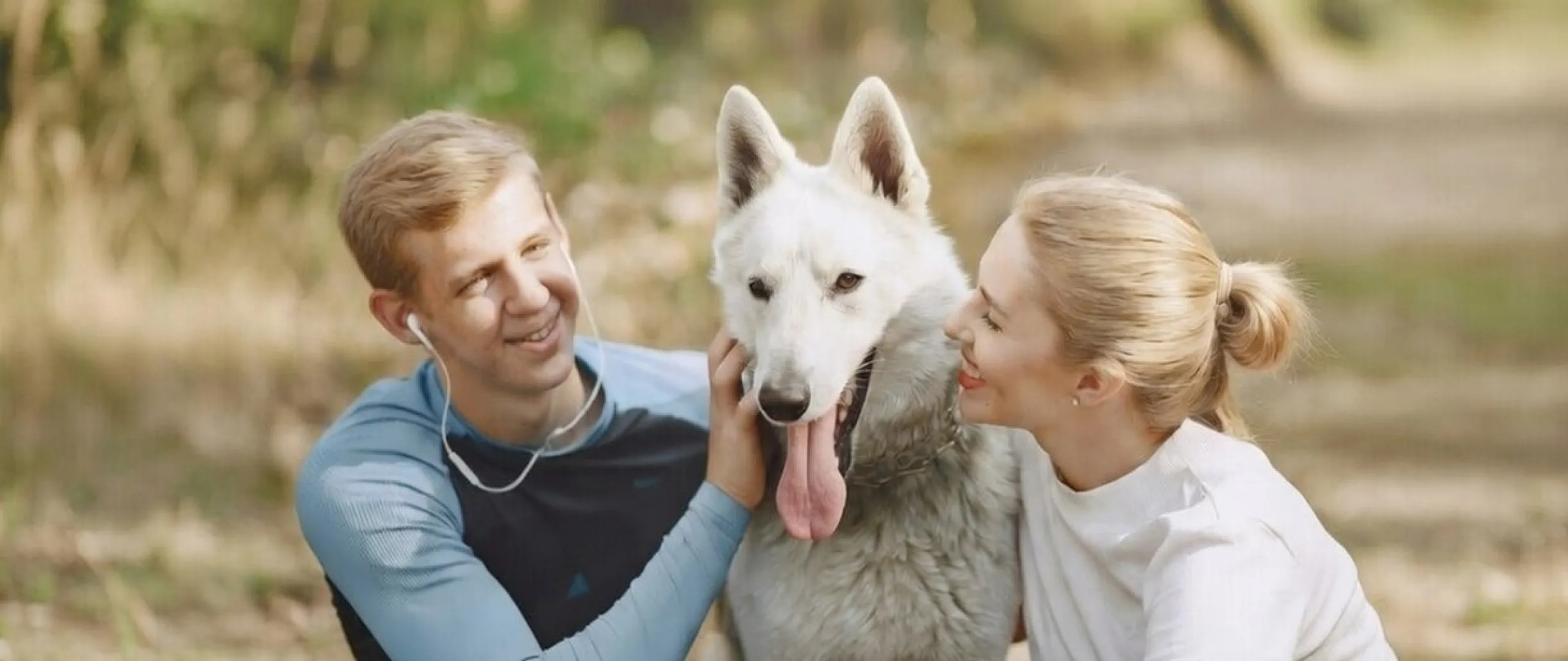Happy couple enjoying a sunny day in the park with their large, friendly dog.
