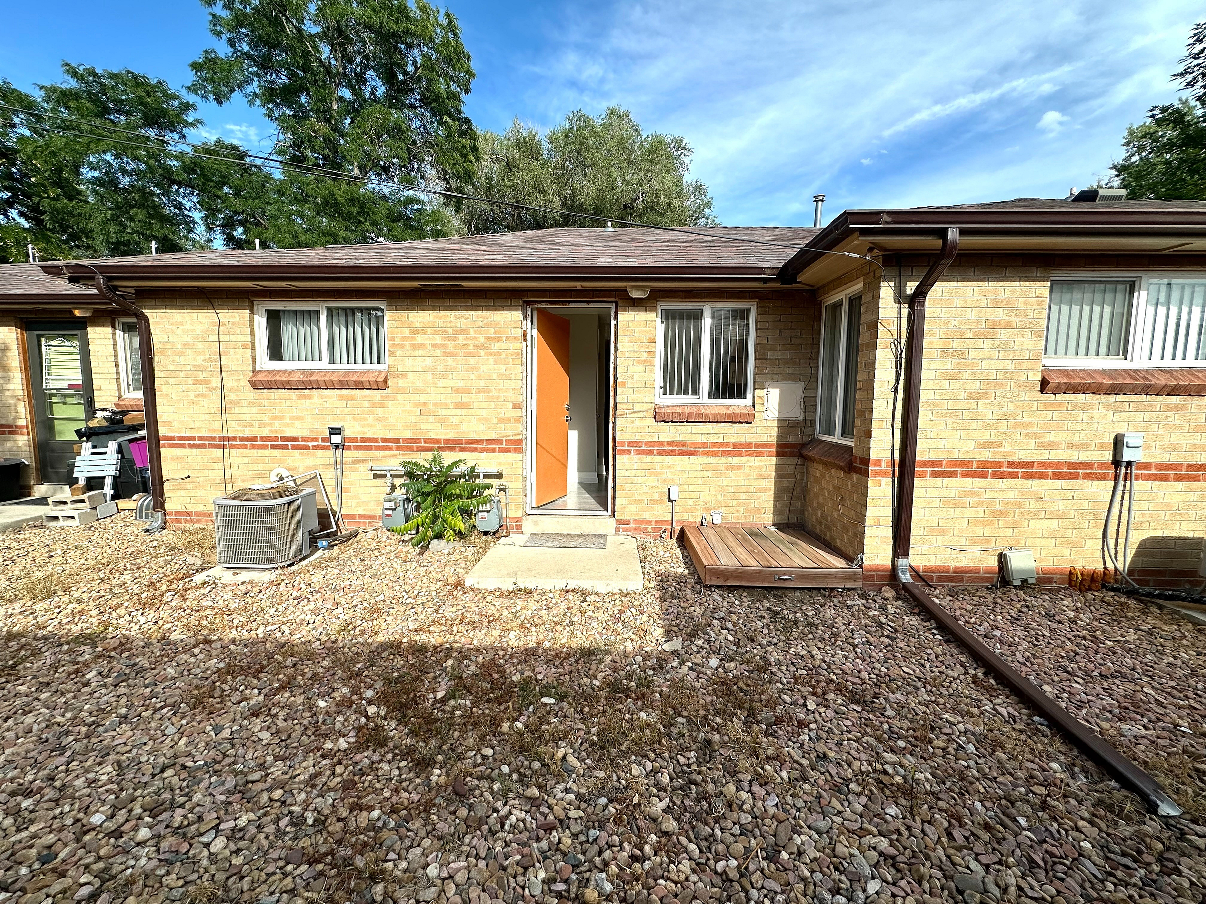 Charming brick exterior of a cozy home with a welcoming open door, surrounded by a low-maintenance rock garden and lush greenery.