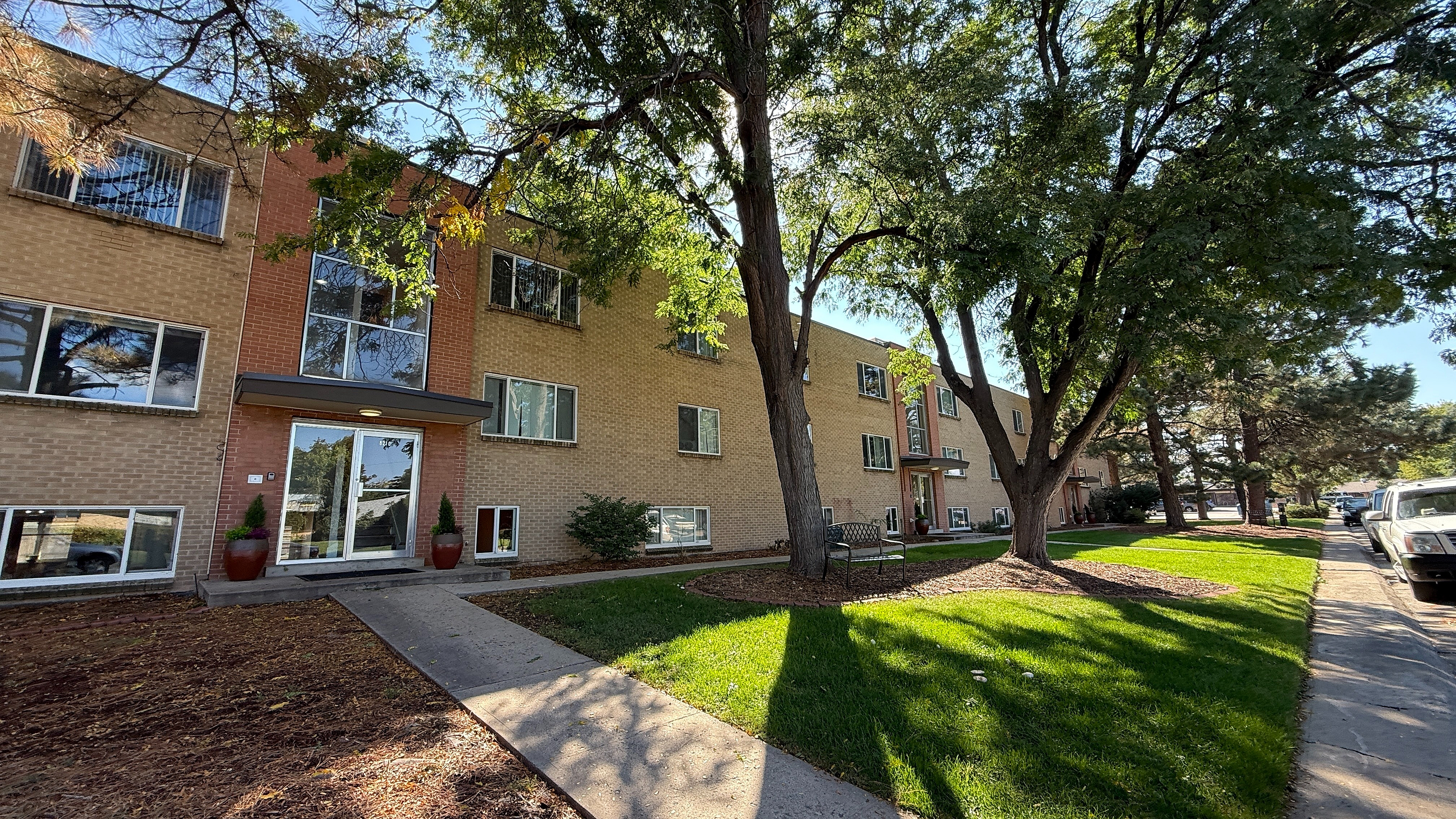 Charming apartment complex with a brick facade, surrounded by lush trees and well-maintained greenery, offering a peaceful urban living environment.
