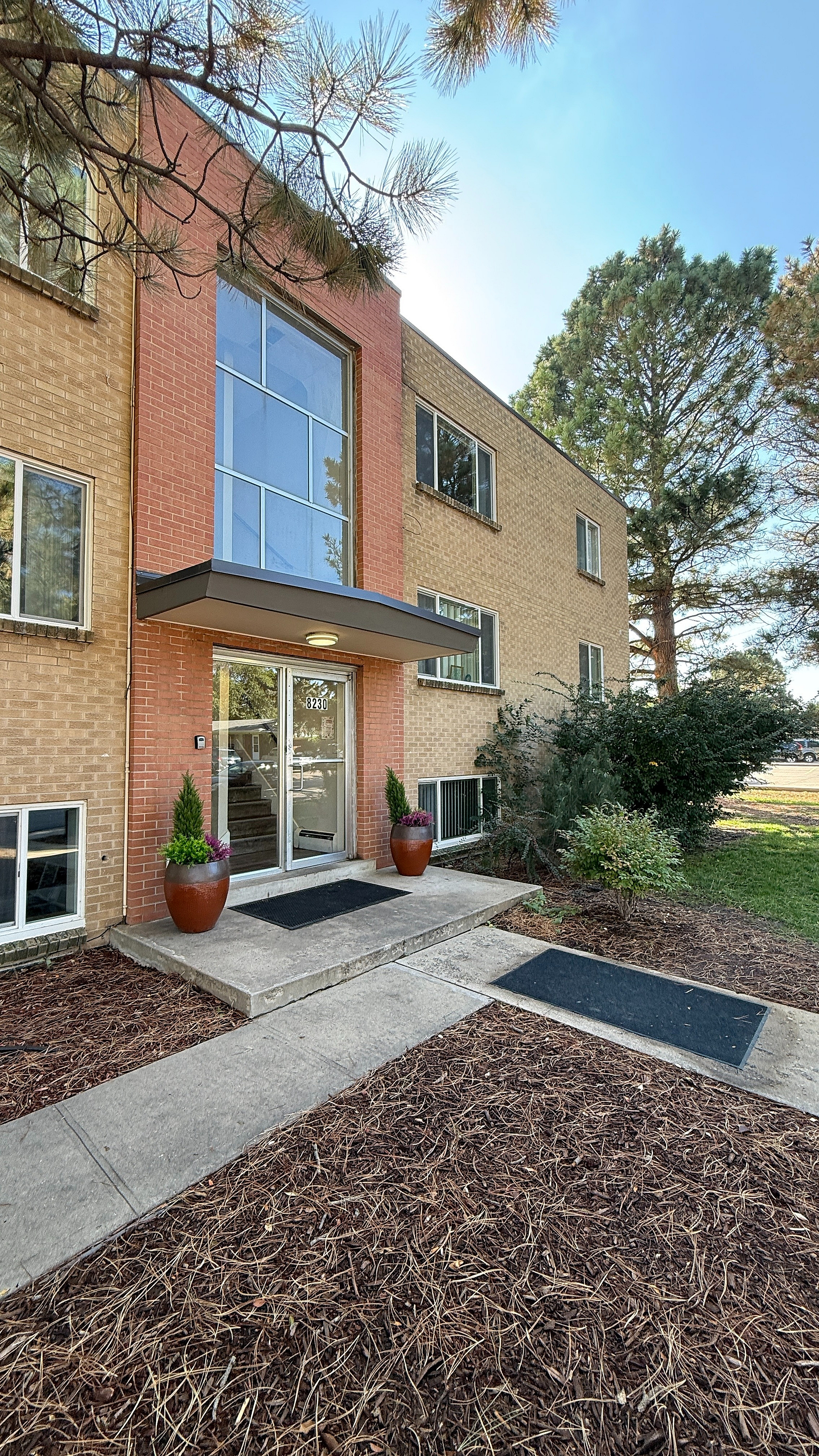 Charming apartment entrance with modern brick facade, large windows, and lovely potted greenery offering a welcoming feel.