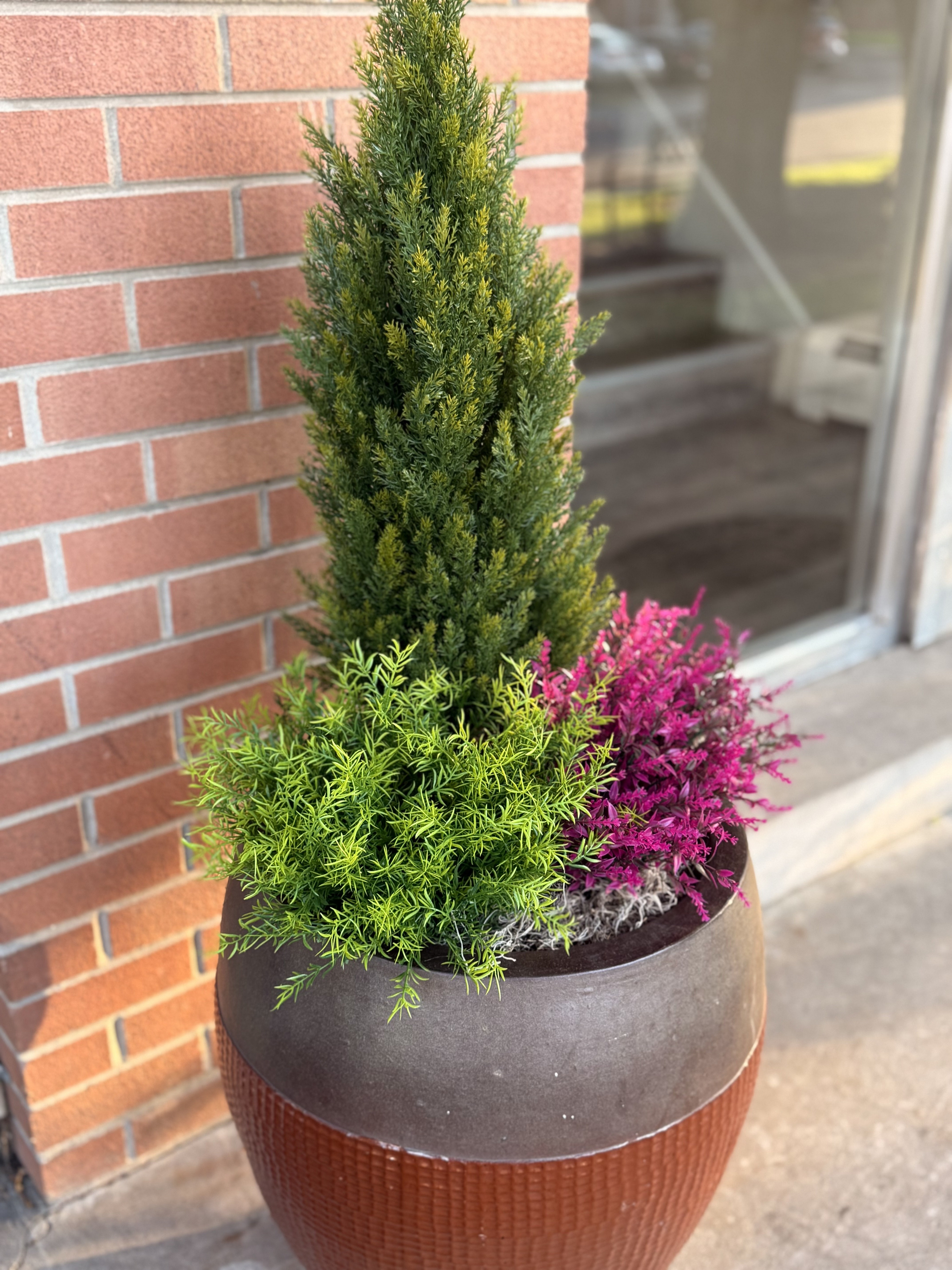 Inviting apartment entrance with a stylish planter featuring lush greenery and vibrant pink flowers, complemented by a charming brick wall backdrop.