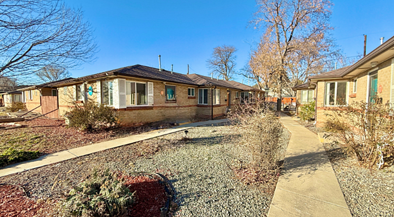 Charming single-story brick apartments surrounded by lush landscaping and tree-lined pathways under a clear blue sky.