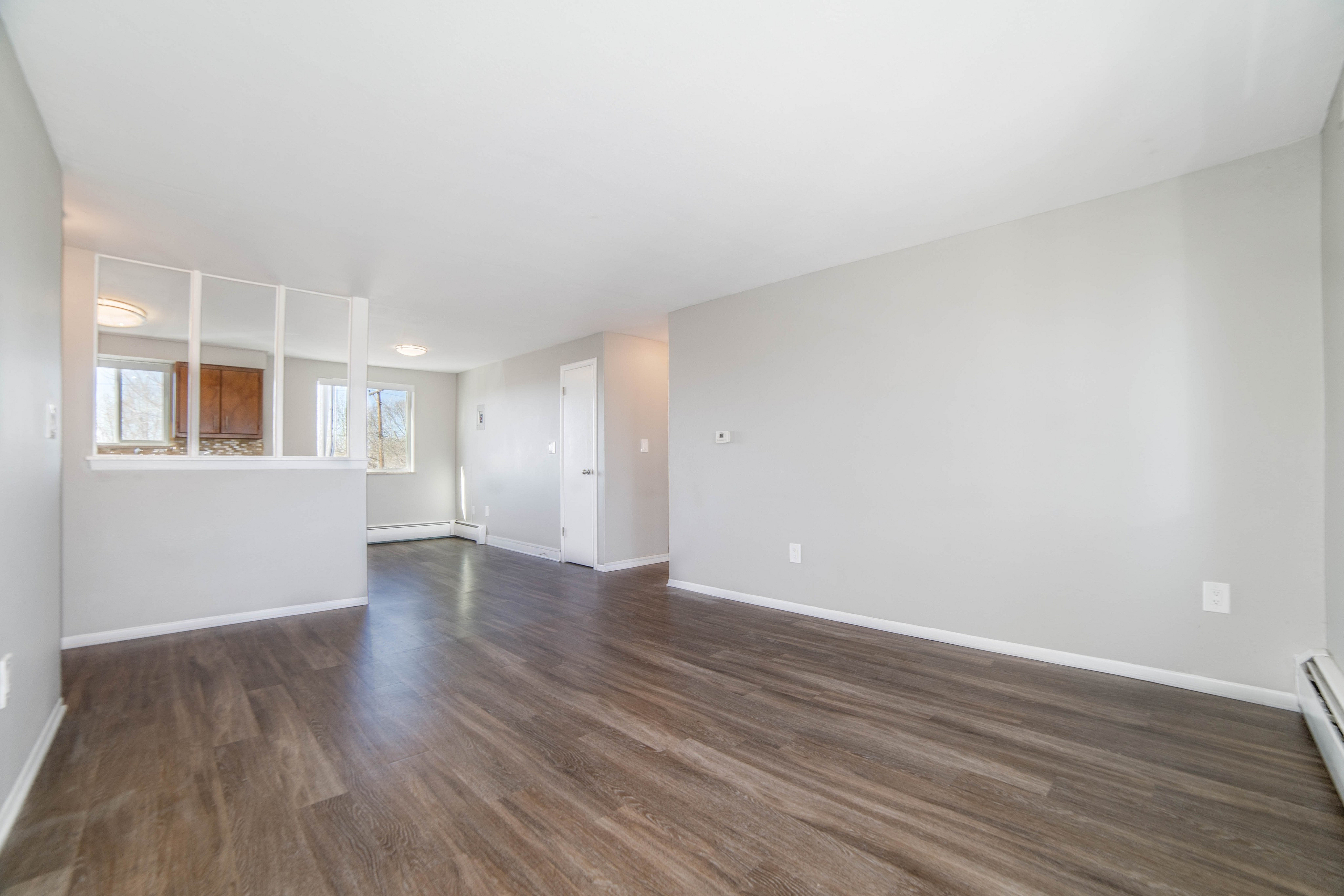 Bright and inviting living space with elegant laminate flooring and a partial view into the kitchen, showcasing modern design and ample natural light.