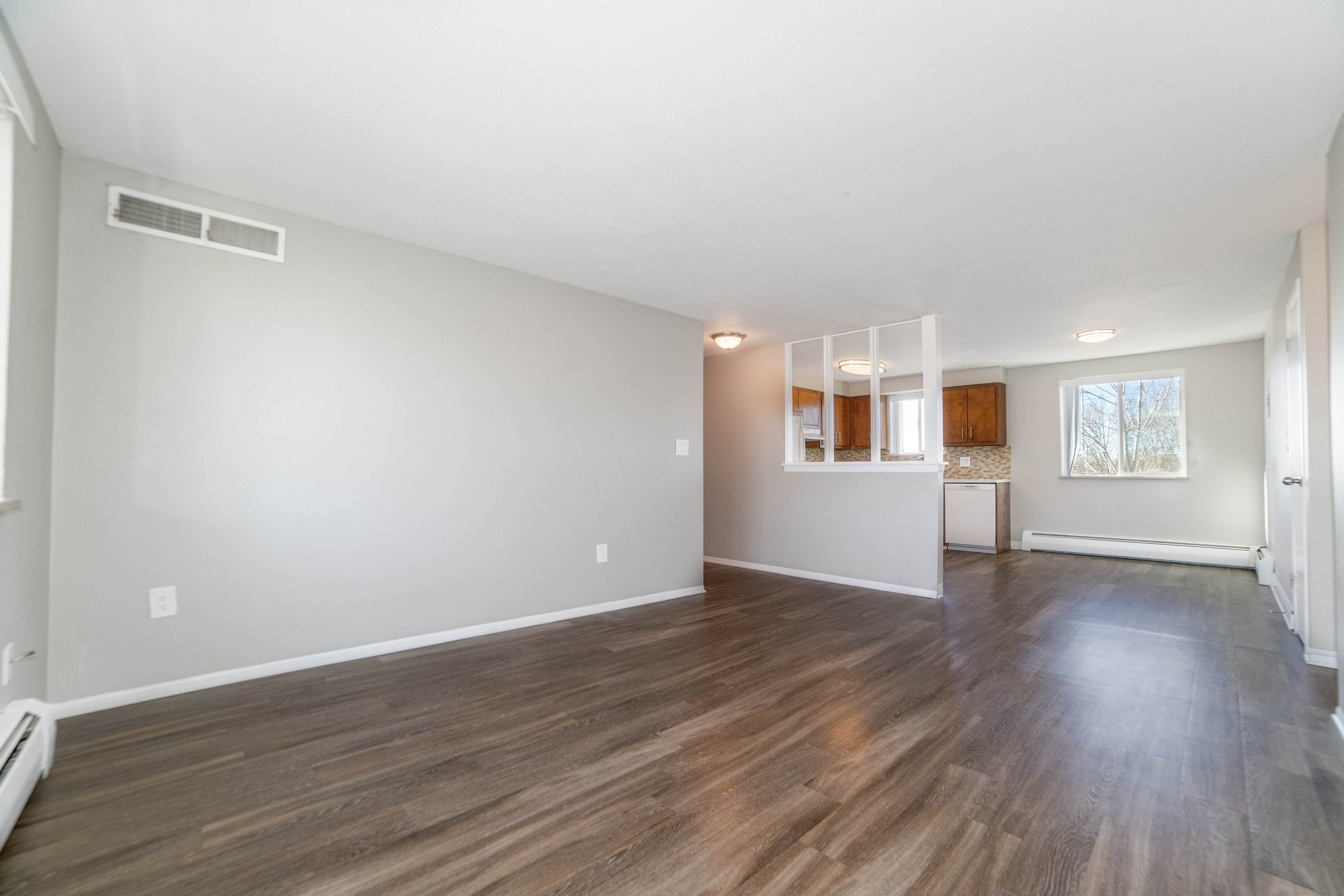 Bright and spacious living area with elegant wood flooring, large windows offering natural light, and a modern, partially open kitchen with sleek cabinetry.