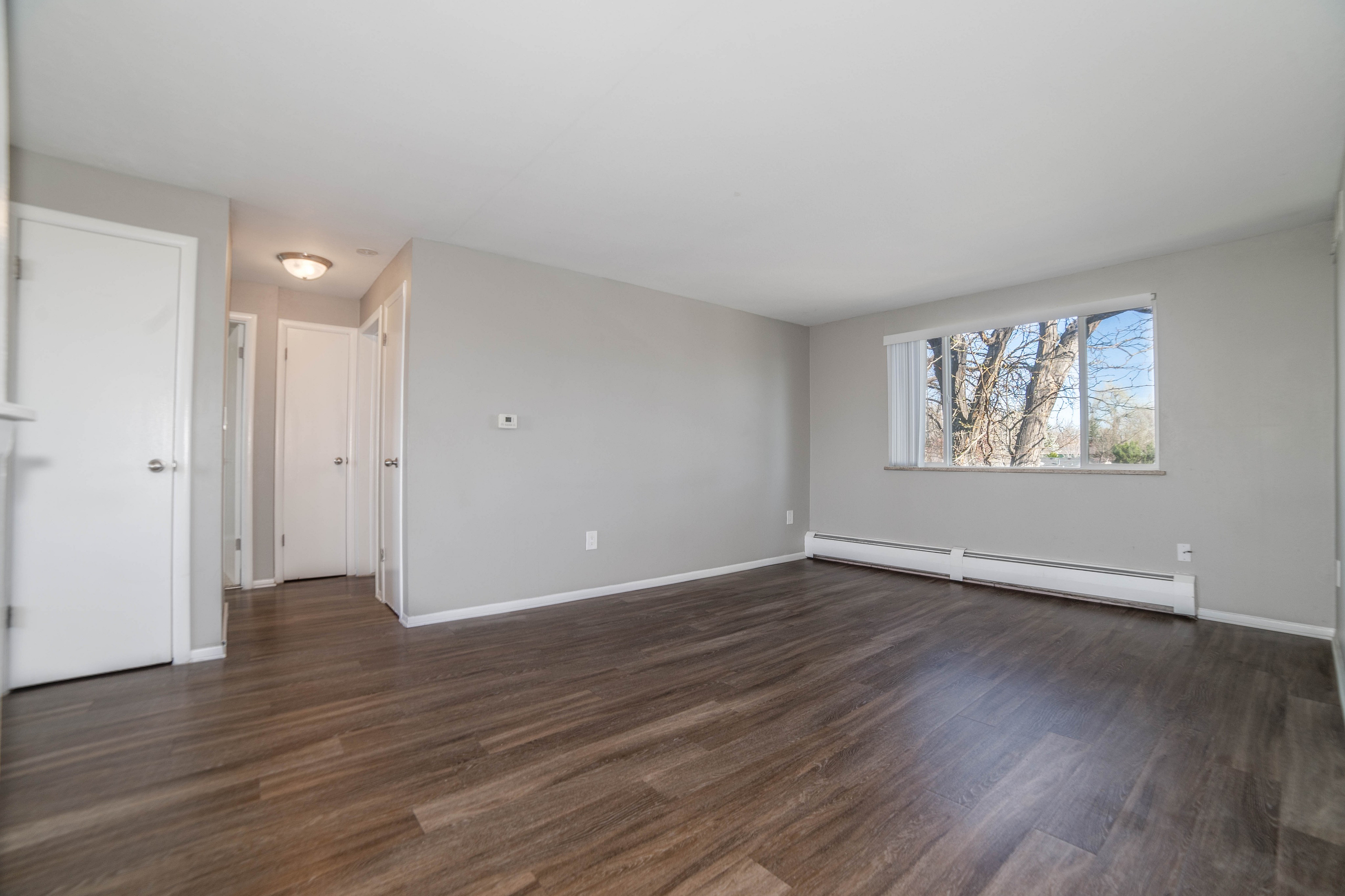 Spacious modern living room with sleek hardwood floors and large window providing plenty of natural light.
