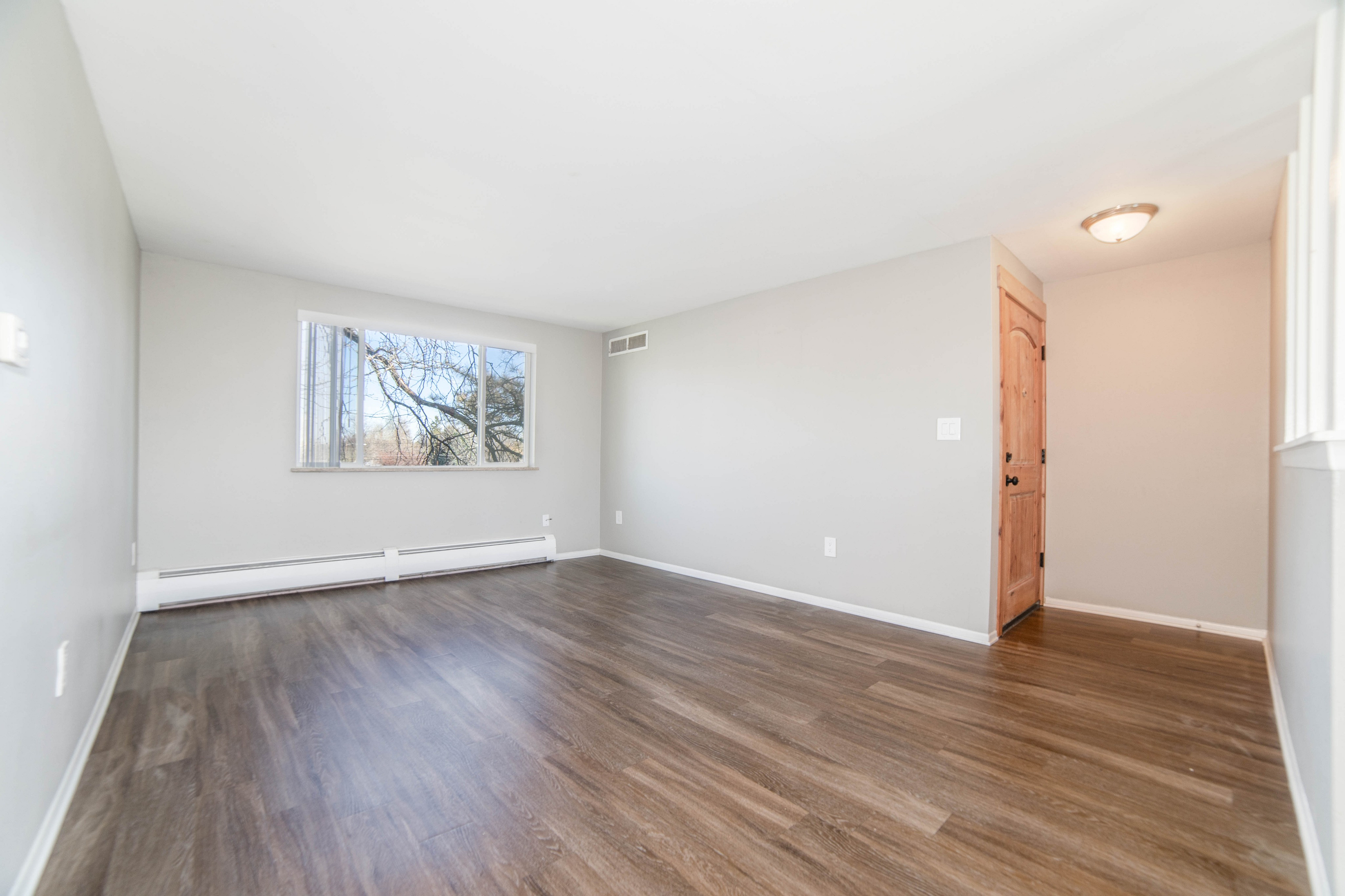 Bright and spacious living area with sleek hardwood floors and large window offering scenic views.
