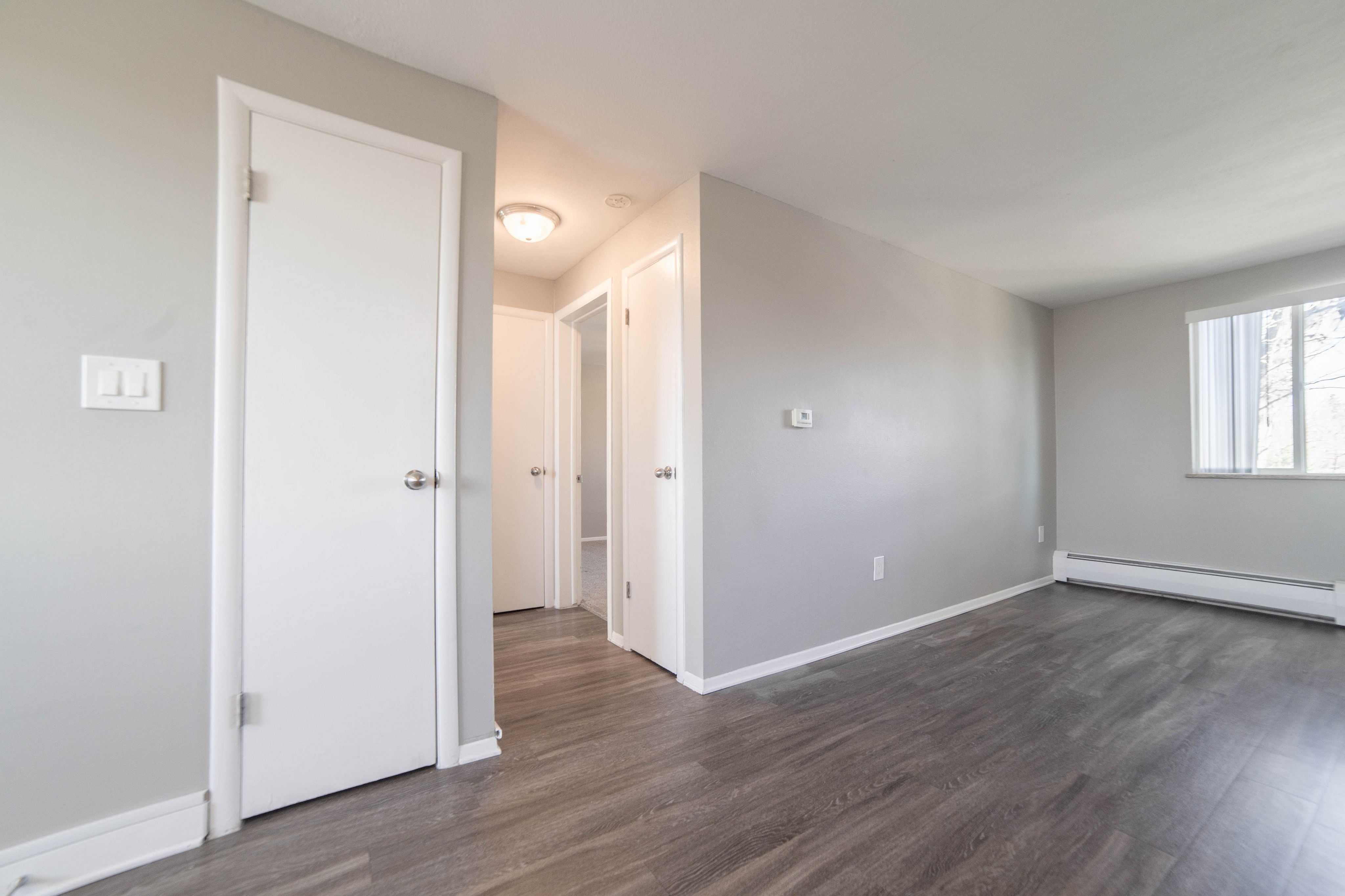 Bright and airy living space with modern gray flooring, soft gray walls, and a large window for ample natural light.