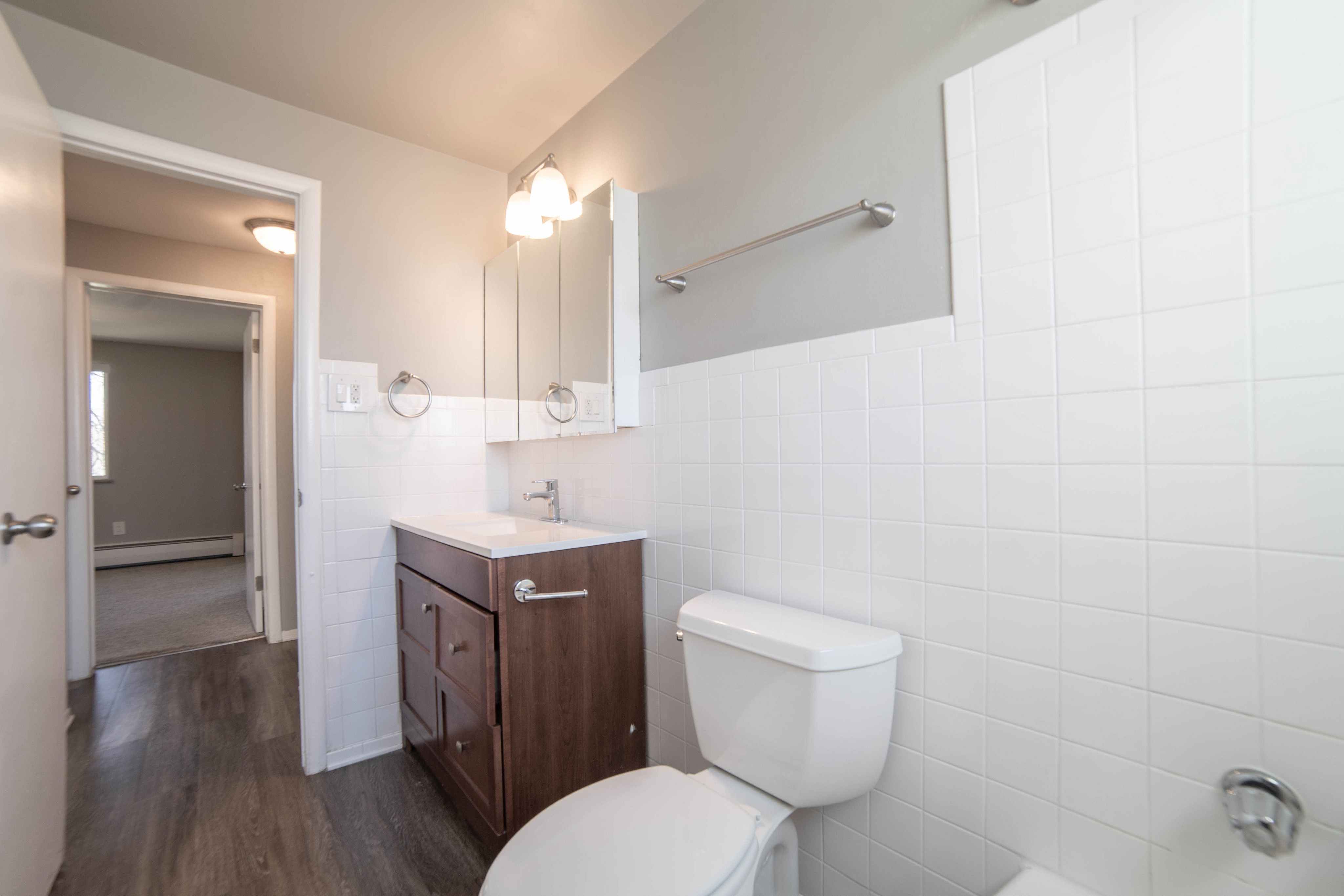 Bright and modern bathroom with elegant fixtures, a sleek wooden vanity, and pristine white tiles, offering a fresh and inviting atmosphere.