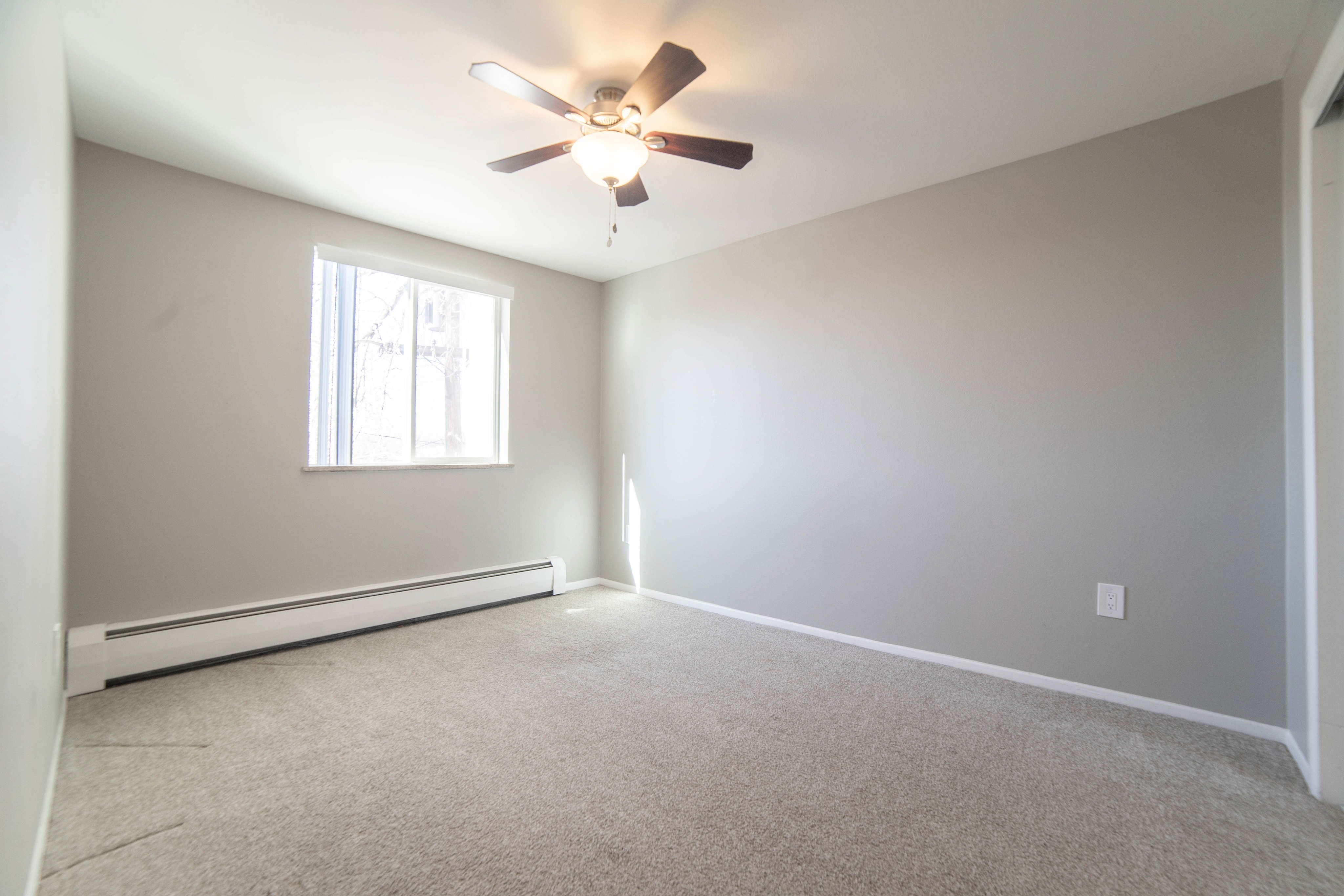 Bright and inviting empty room with neutral walls, soft carpet, and a modern ceiling fan, ready to be personalized.