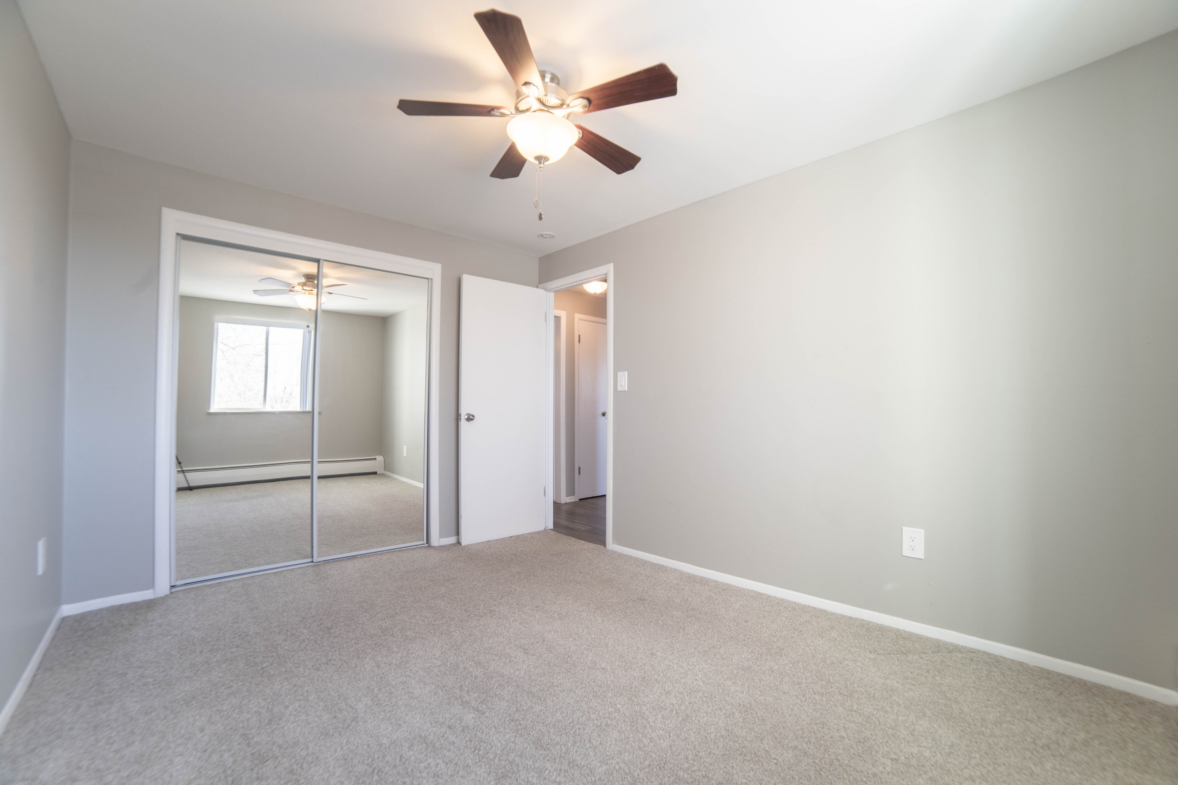Bright and airy bedroom with plush carpeting, mirrored closet doors, and a modern ceiling fan.