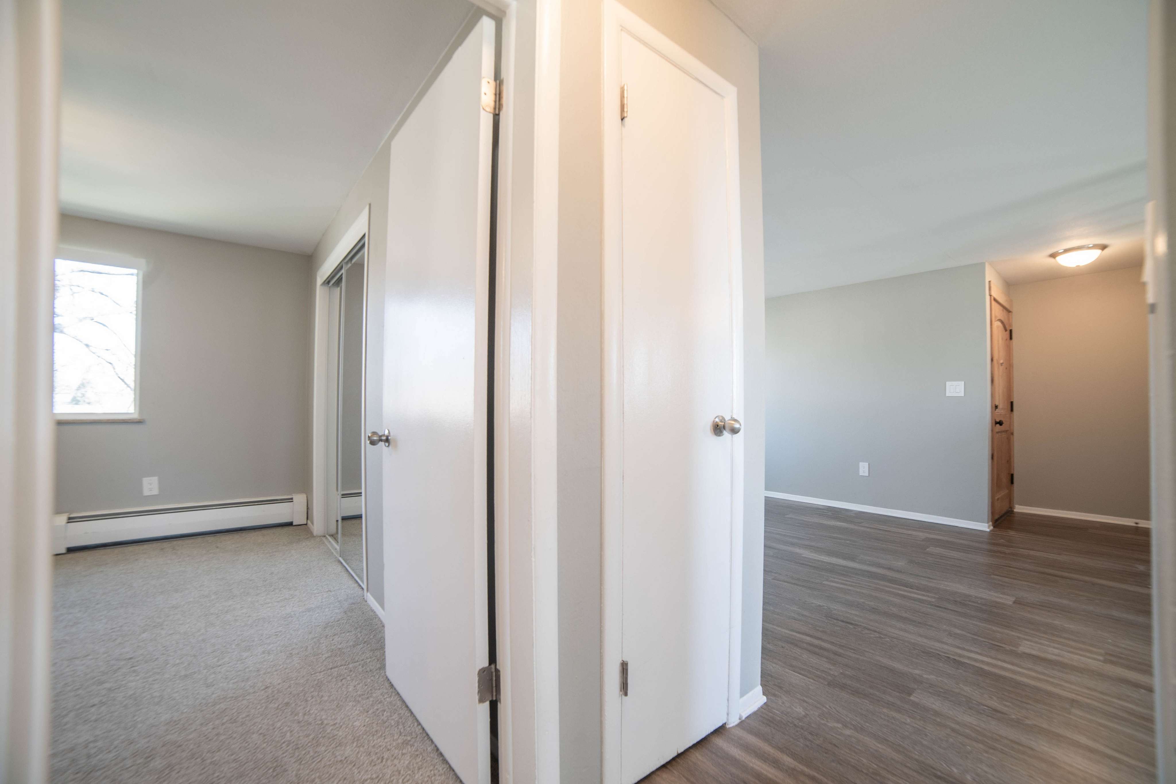 Modern apartment hallway featuring elegant wooden flooring, bright natural light, and doors leading to spacious rooms.