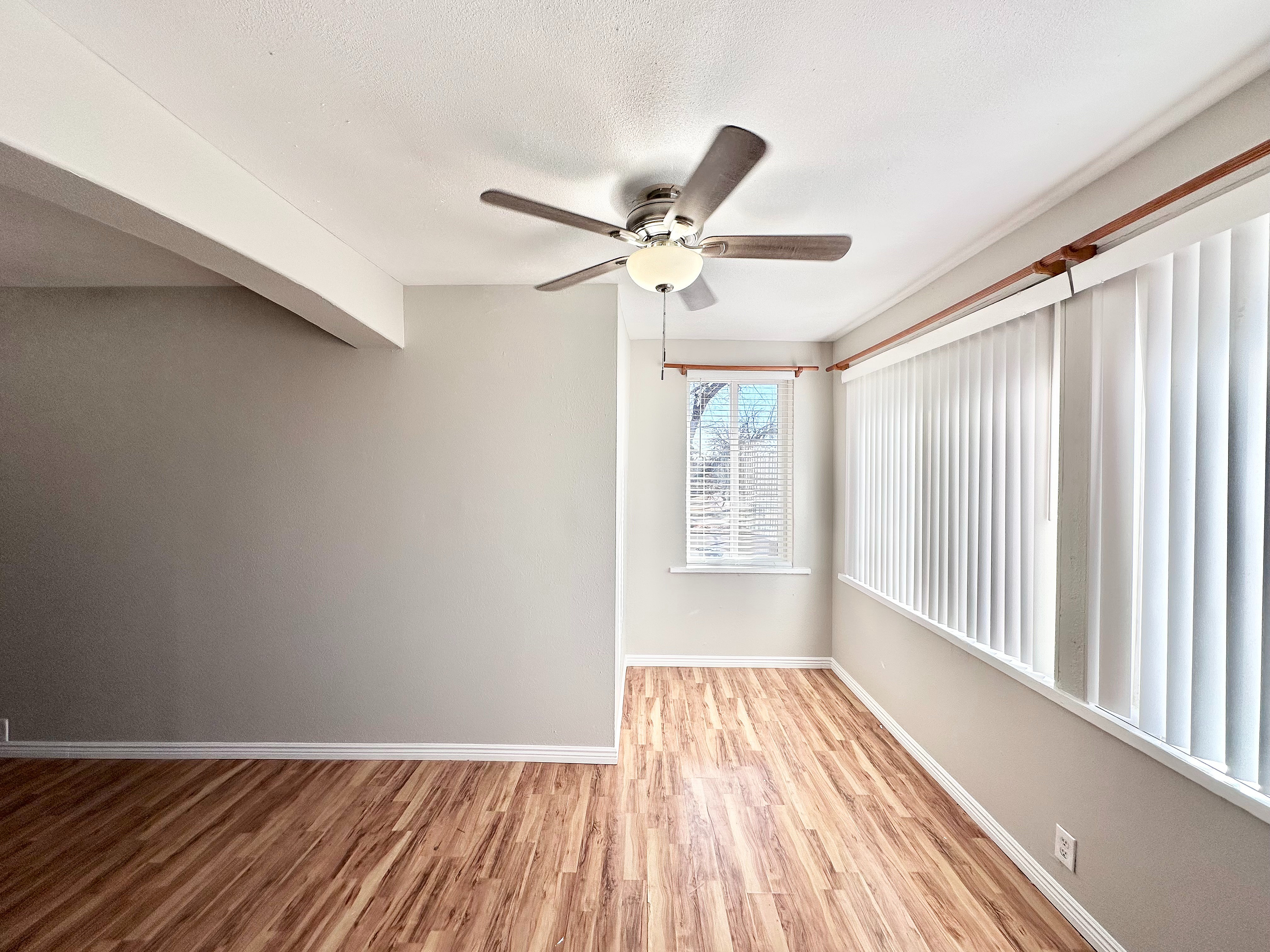 Bright and airy living space with elegant wood flooring and large windows, complemented by a modern ceiling fan for a perfect blend of comfort and style.