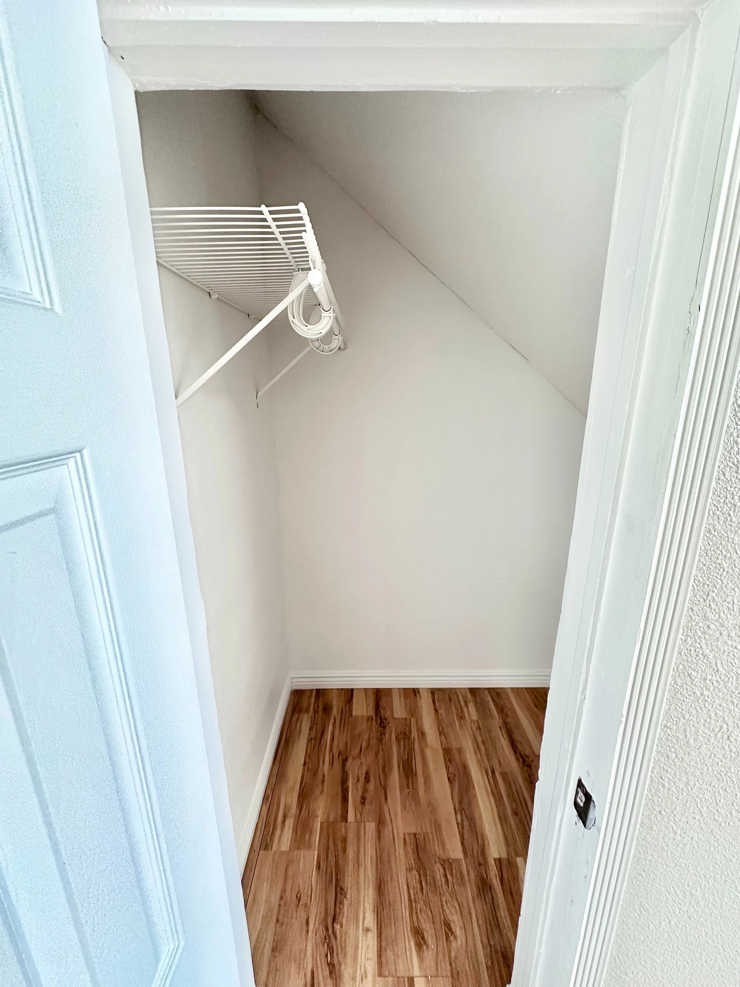 Cozy closet space with elegant hardwood flooring and a sleek white wire shelf, perfect for stylish organization.