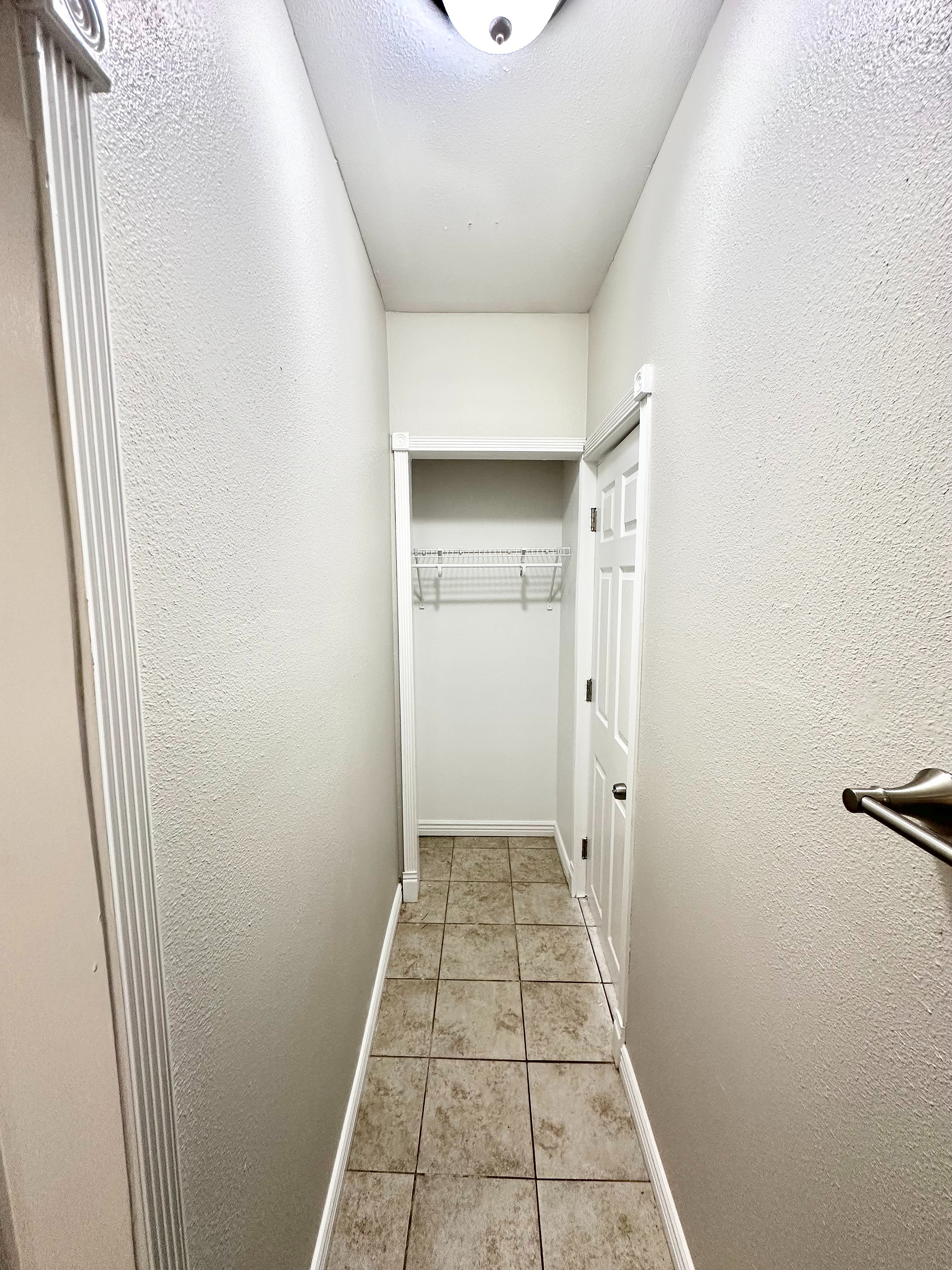 Bright, inviting hallway featuring elegant tile flooring and a modern light fixture, leading to a convenient closet space.