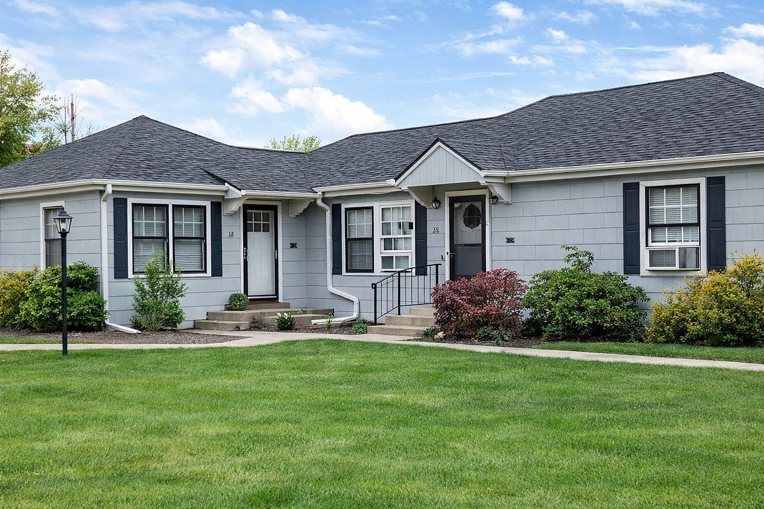 Charming duplex with classic architecture, pristine landscaping, and inviting entryways surrounded by lush greenery.