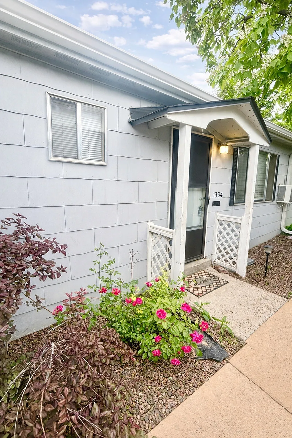 Charming home entrance with vibrant flowers, elegant siding, and welcoming porch under a clear blue sky.
