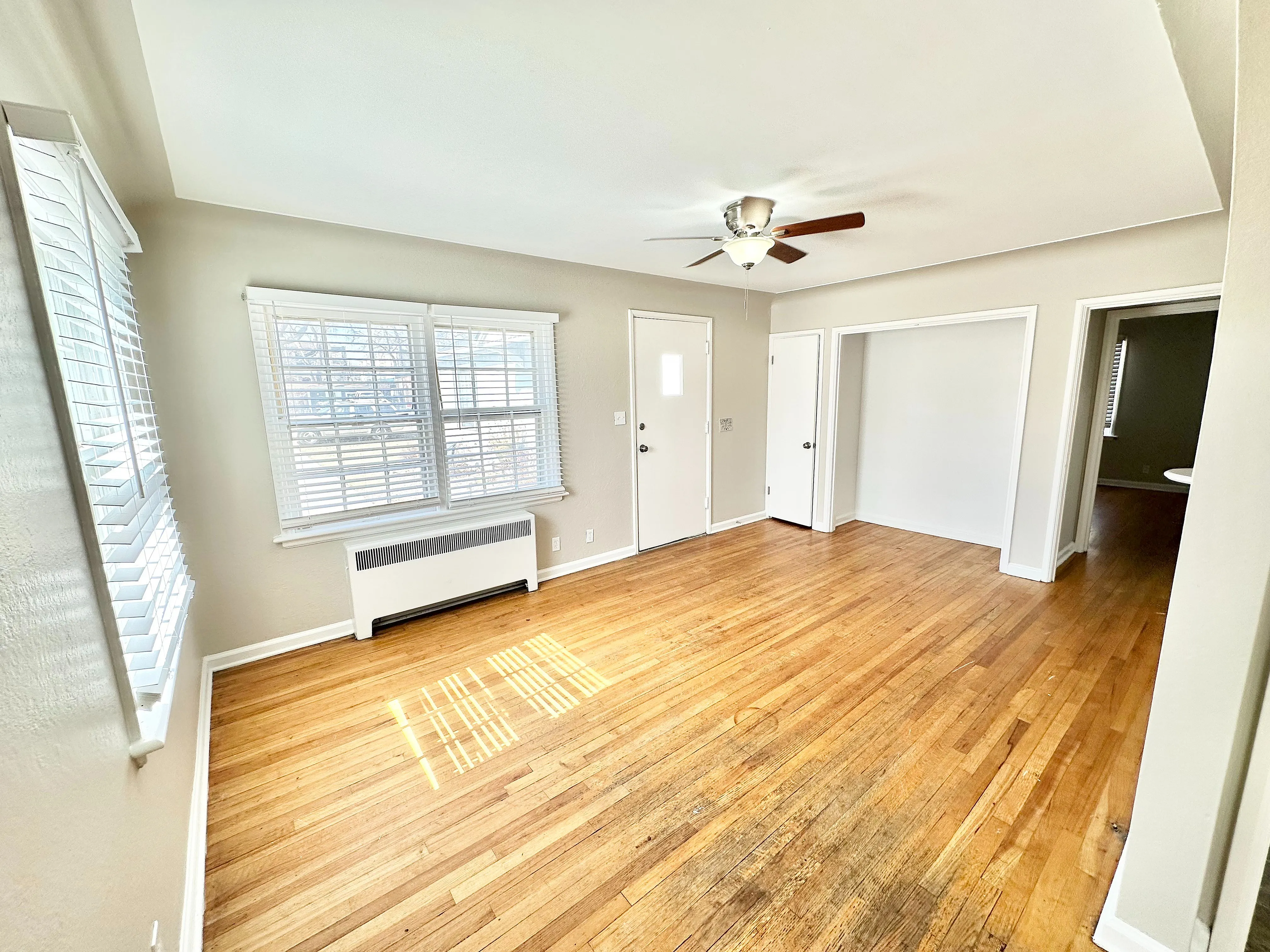 Bright, airy living space with hardwood floors, featuring large windows and modern ceiling fan, perfect for cozy gatherings.