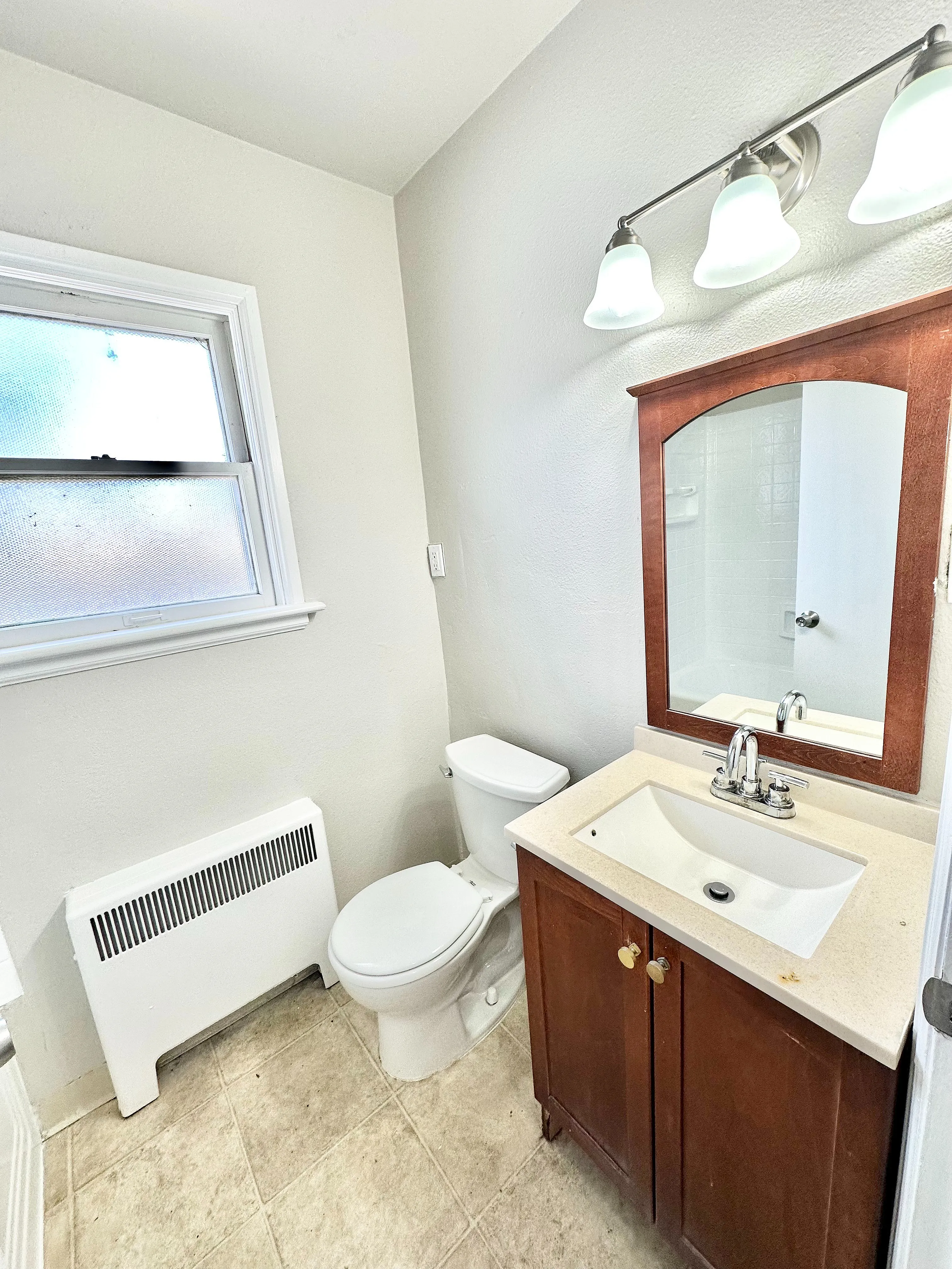 Bright and modern bathroom with elegant lighting, polished mirror, and rich wooden vanity.