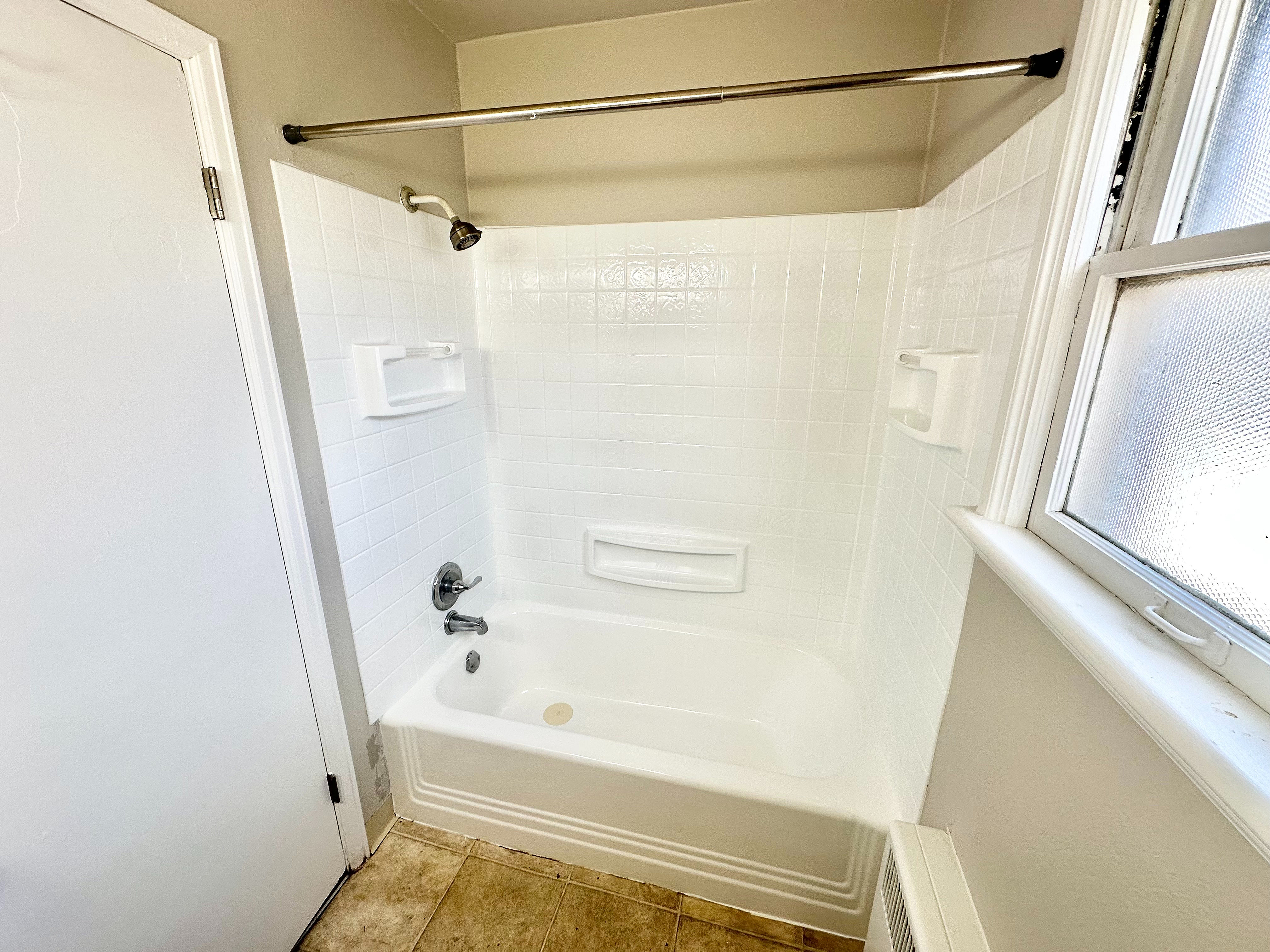 Bright and pristine bathroom featuring a gleaming white tiled bathtub with built-in shelves and a modern window for natural light.