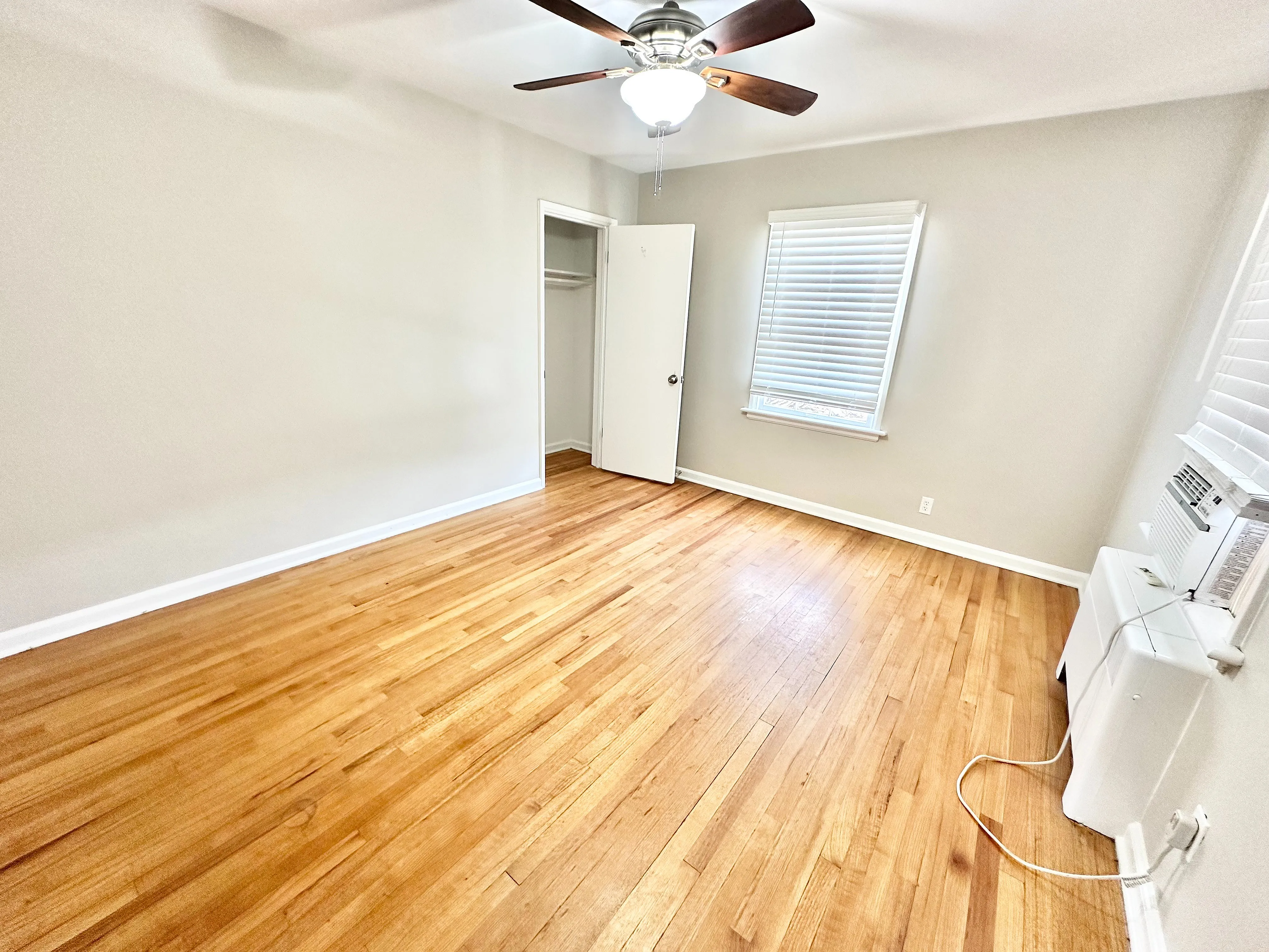 Bright and airy room with elegant wood flooring, a modern ceiling fan, and a convenient closet space, perfect for a cozy bedroom setup.