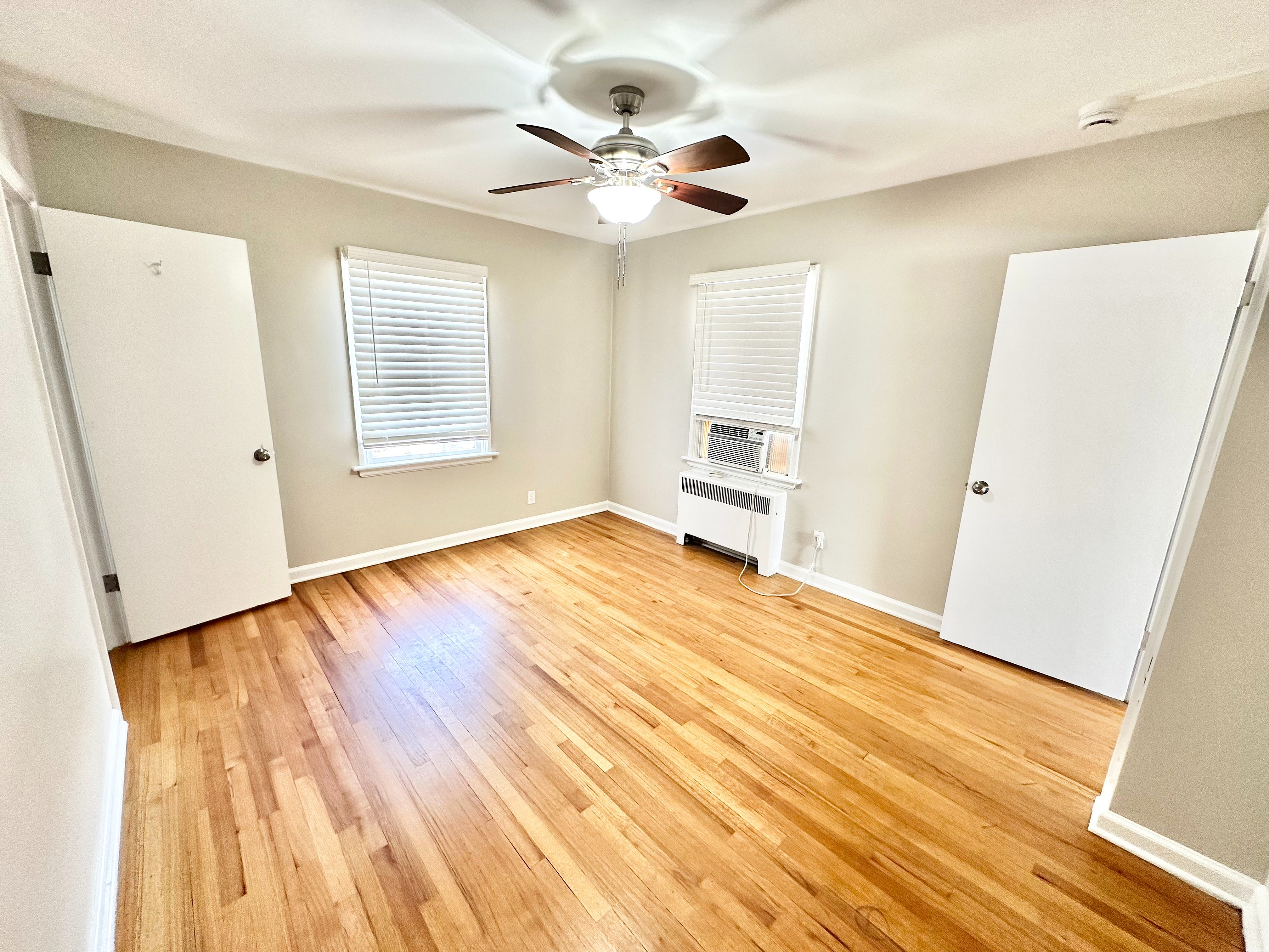 Bright and airy room with polished hardwood floors, ceiling fan, and ample natural light, perfect for comfortable living.