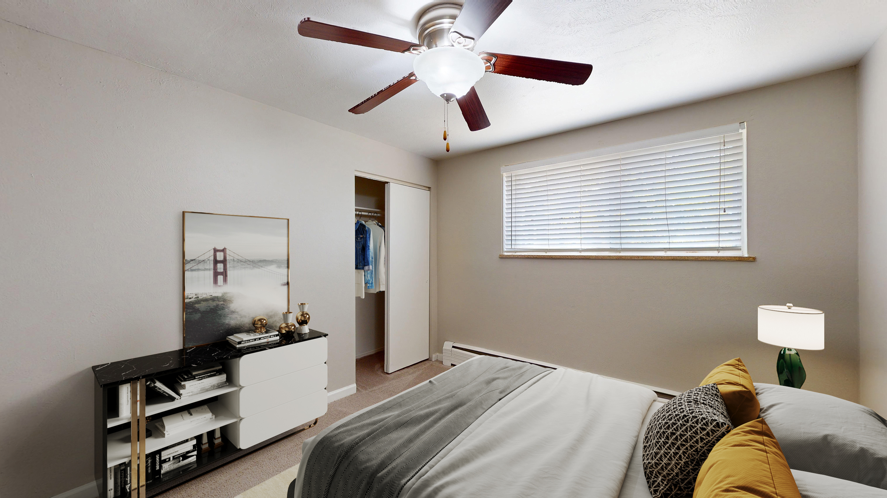 Bright bedroom with modern ceiling fan, cozy bed with stylish cushions, and ample natural light filtering through blinds.