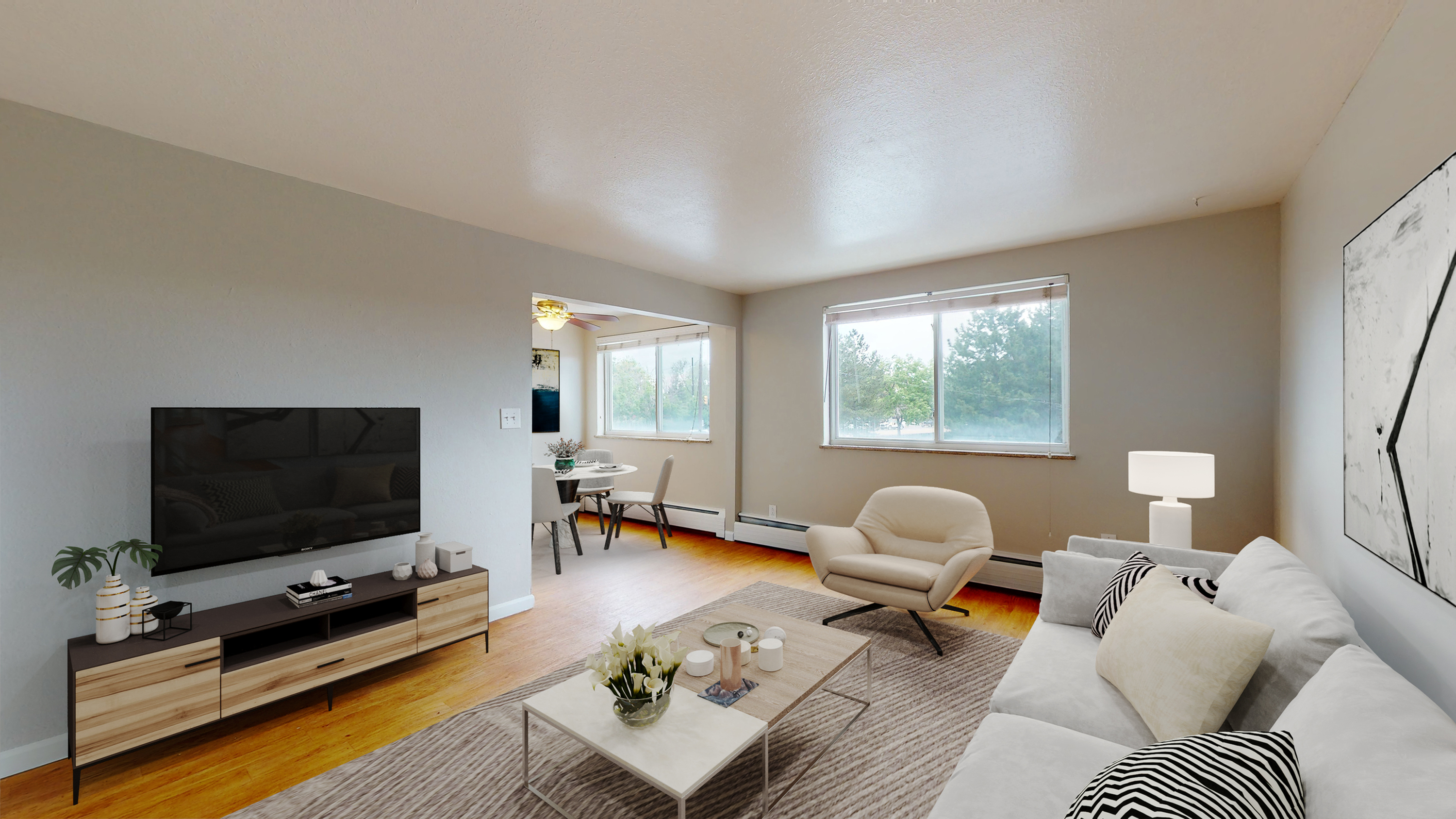 Bright open-plan living room with cozy seating, modern TV setup, and dining area, enhanced by large windows and stylish décor.