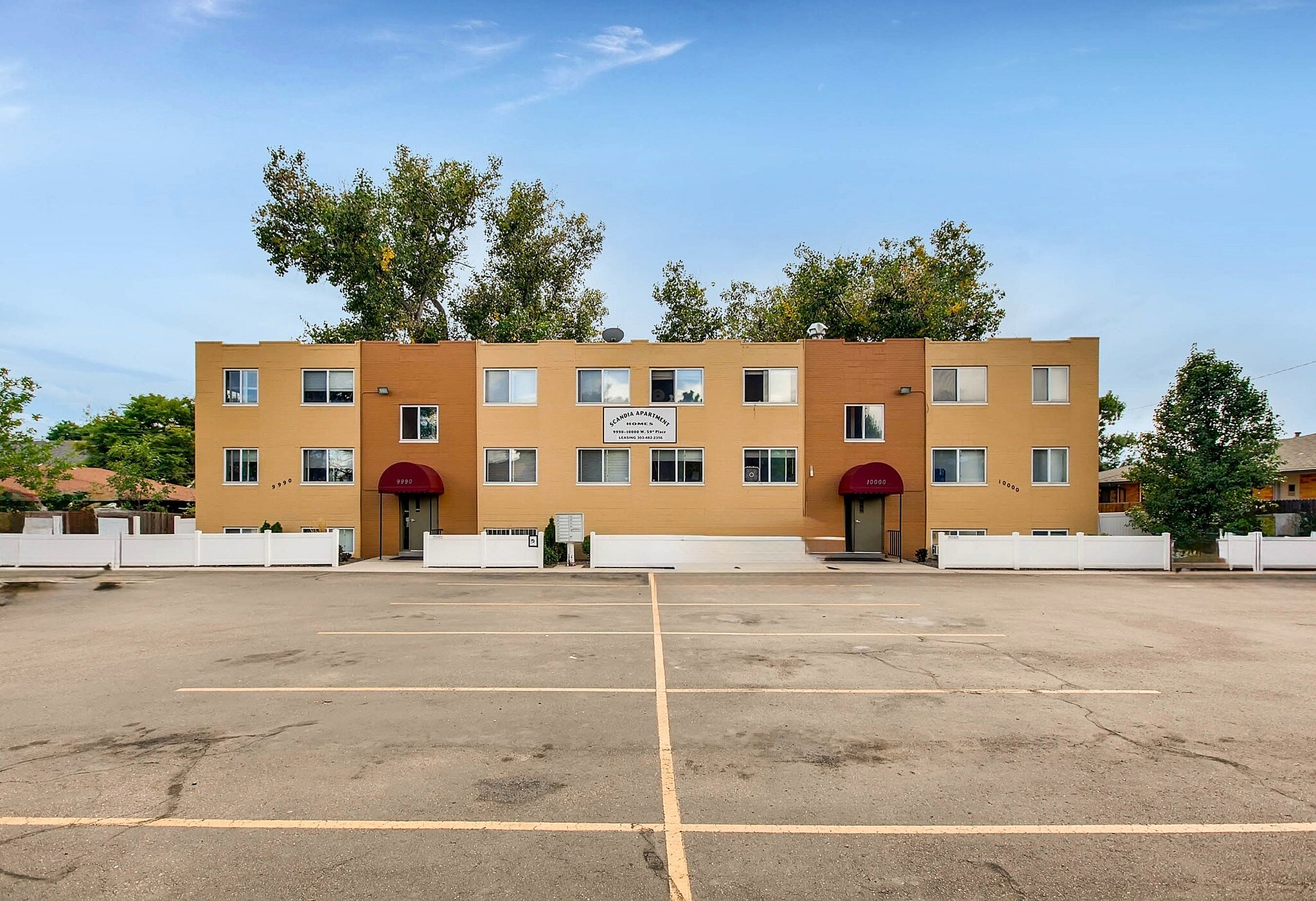 Bright and inviting apartment building with a welcoming entrance, surrounded by lush greenery and ample parking space.
