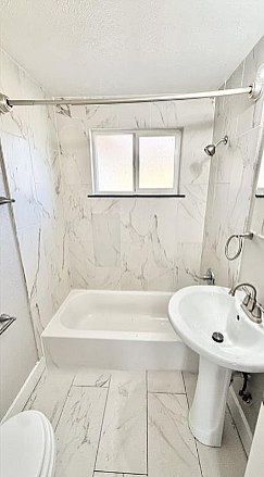 Elegant bathroom featuring a modern bathtub with sleek fixtures, a chic pedestal sink, and bright natural lighting.