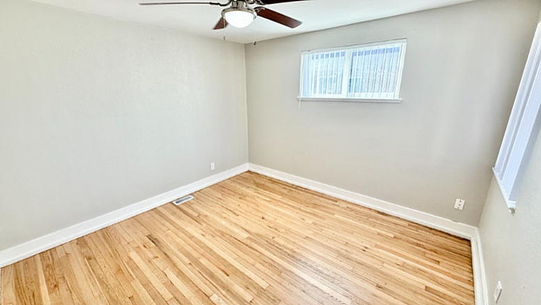 Bright, spacious room with polished hardwood floors and natural light from a wide window, perfect for a cozy bedroom or home office.