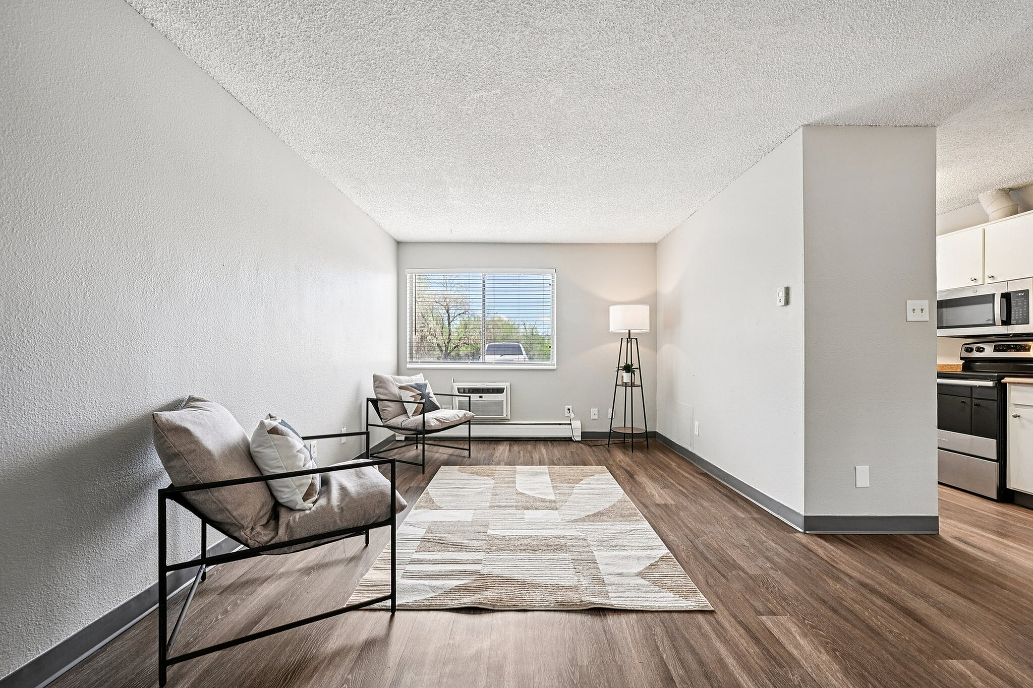 Bright and airy living space showcasing modern seating, large window with natural light, and open floor plan leading to a contemporary kitchen.