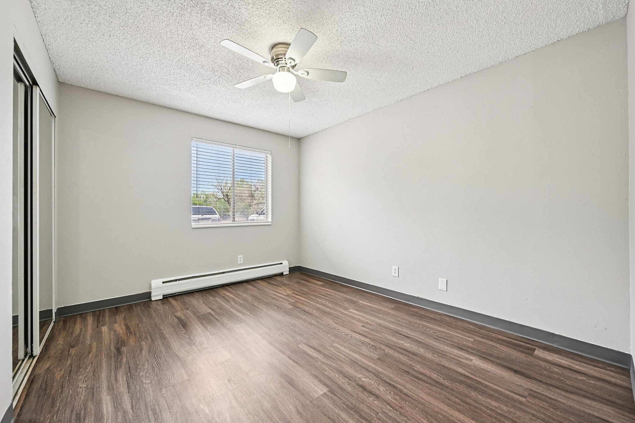 Bright and spacious bedroom with elegant wood flooring, a large window offering ample natural light, and a ceiling fan for comfort.