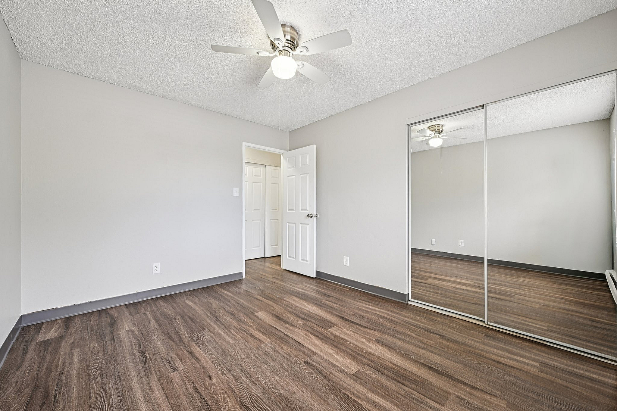 Bright and spacious bedroom with elegant wood flooring, mirrored closet doors, and a modern ceiling fan.