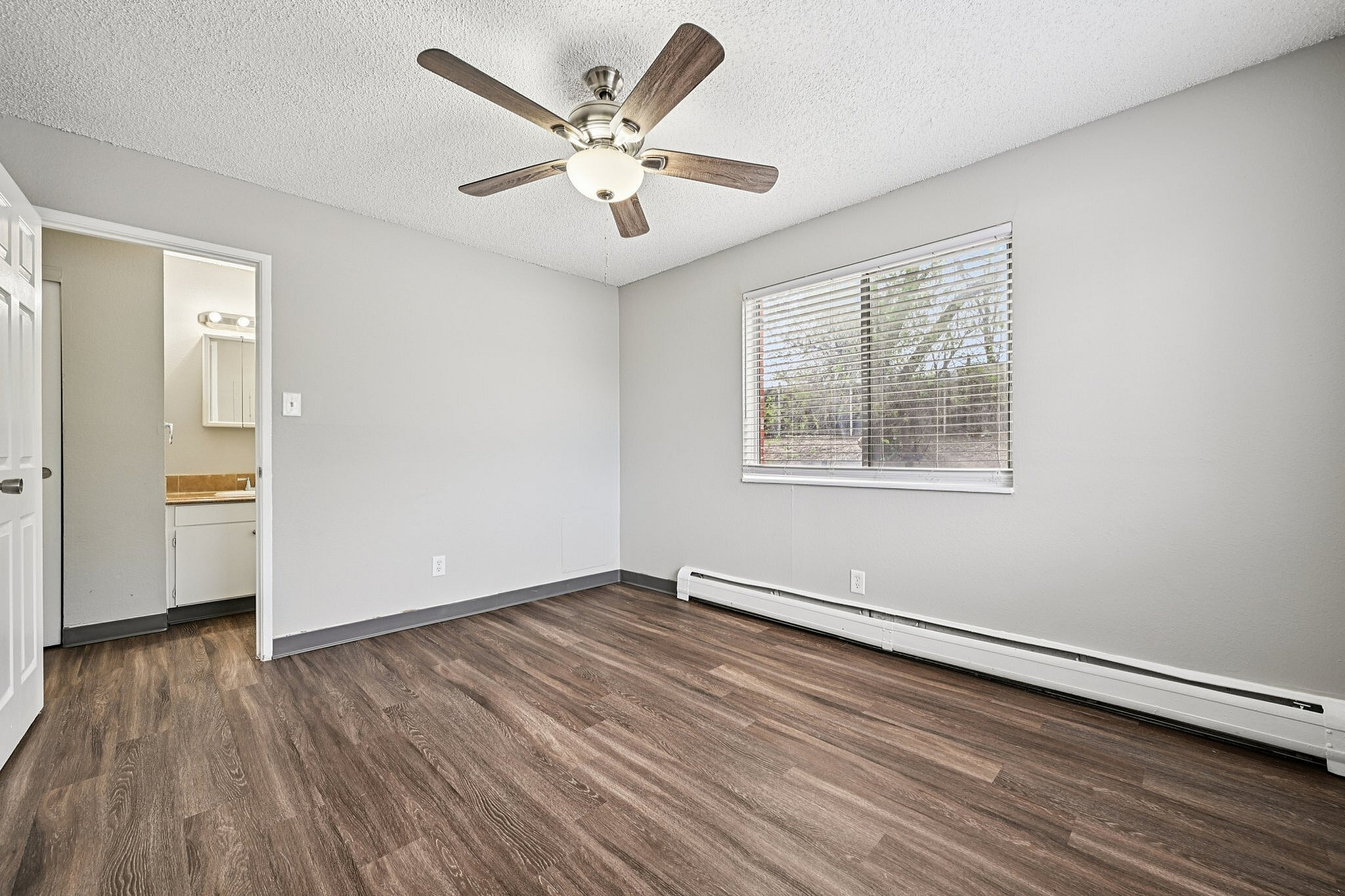 Bright and airy bedroom with modern ceiling fan, large window bringing in natural light, and elegant wood flooring.