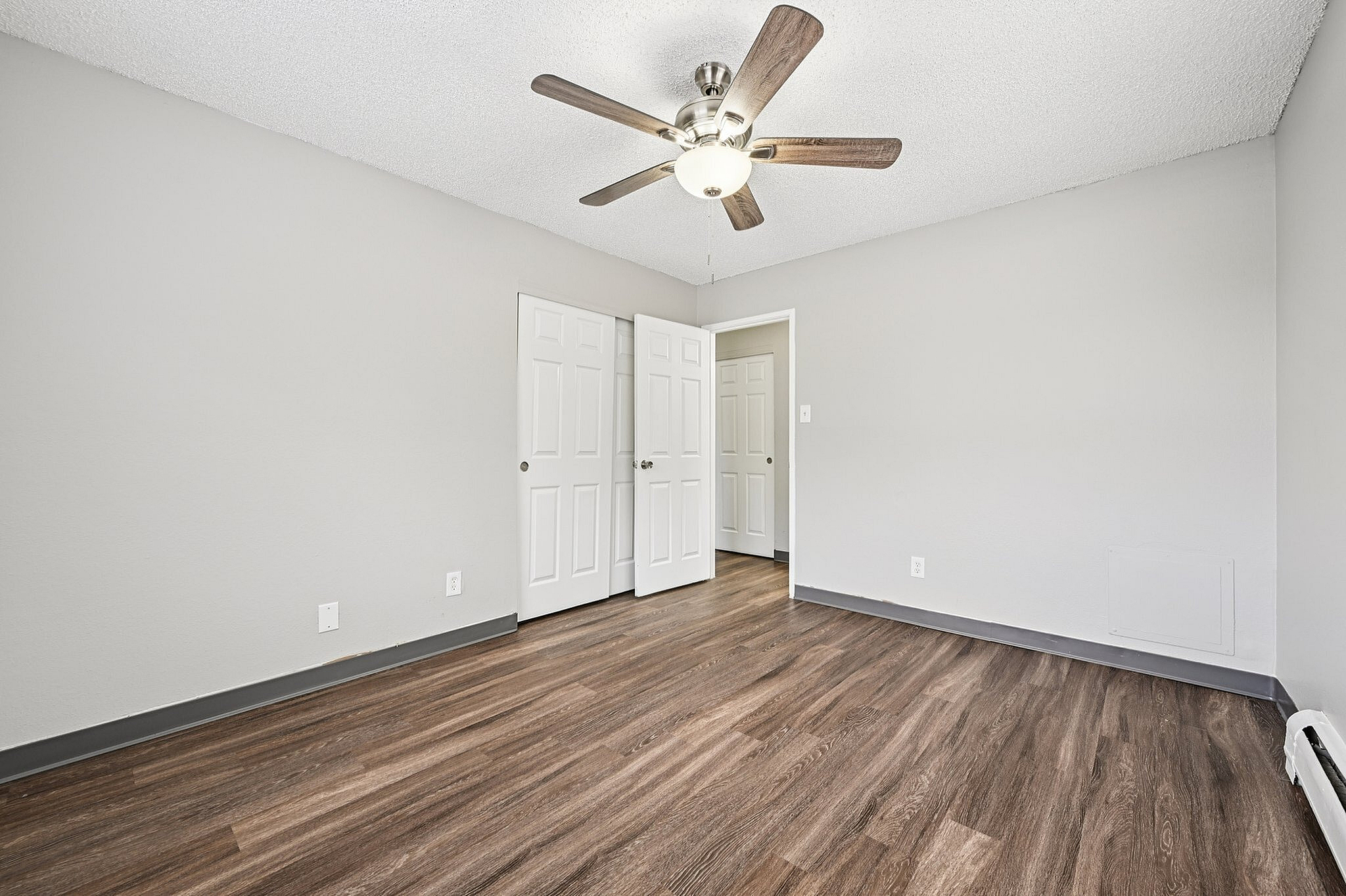 Bright room with elegant wood flooring, pristine white doors, and a modern ceiling fan, perfect for comfortable living.