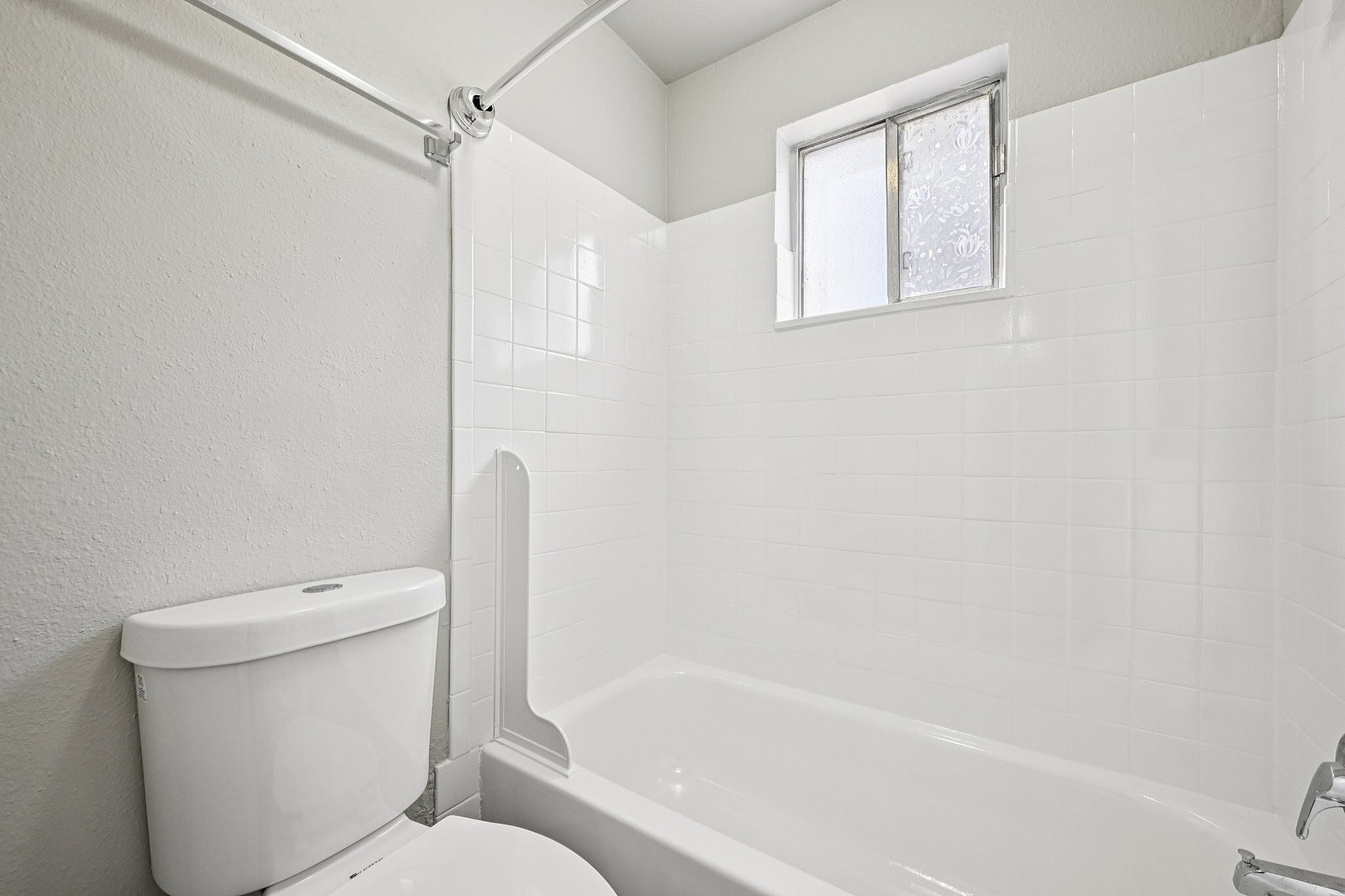 Bright, modern bathroom with sleek white tiles, a spacious bathtub, and a frosted window for natural light.