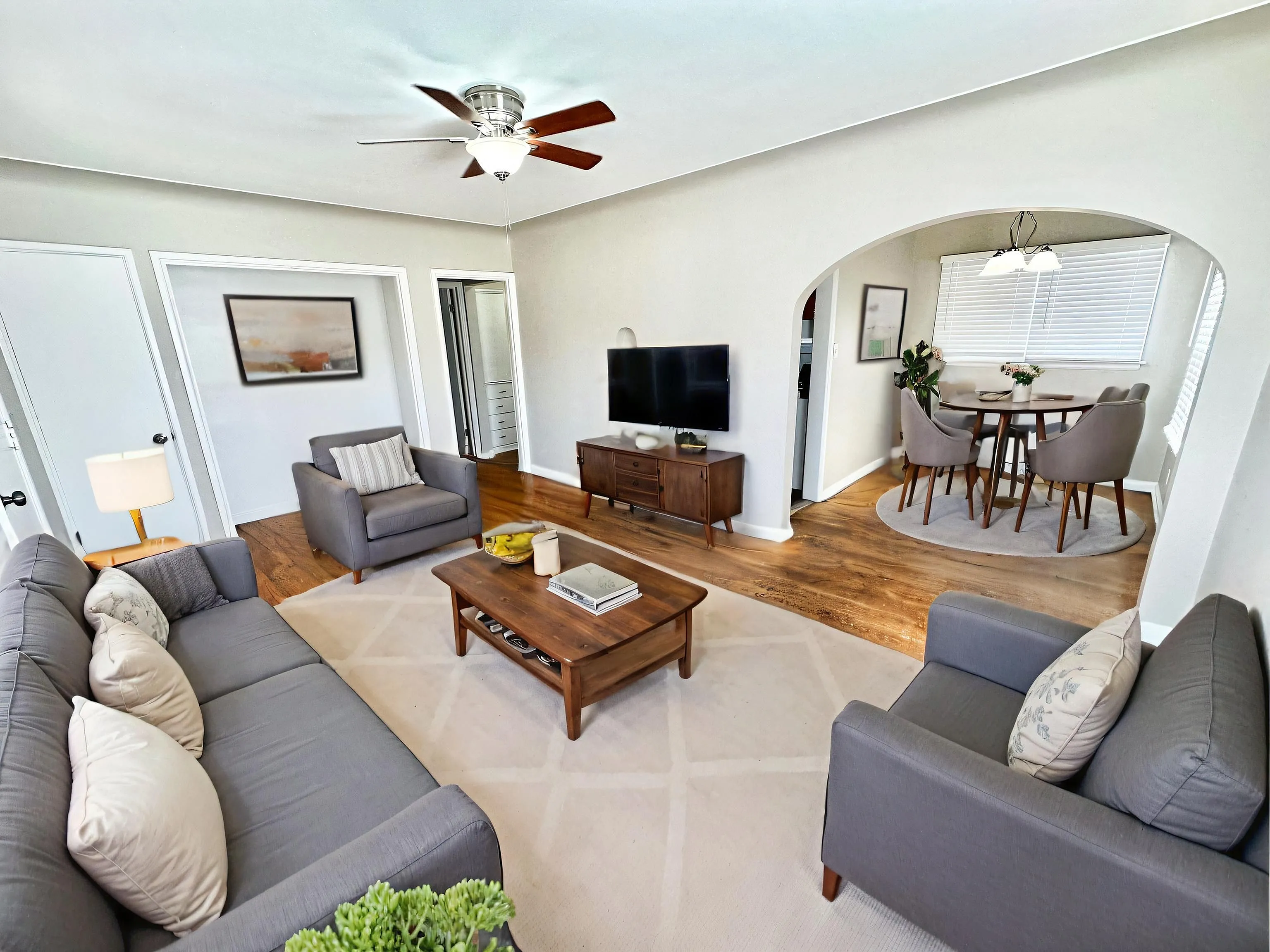 Charming living room with elegant gray sofas, wooden coffee table, and a stylishly integrated dining area featuring a round table and plush chairs under ambient lighting.