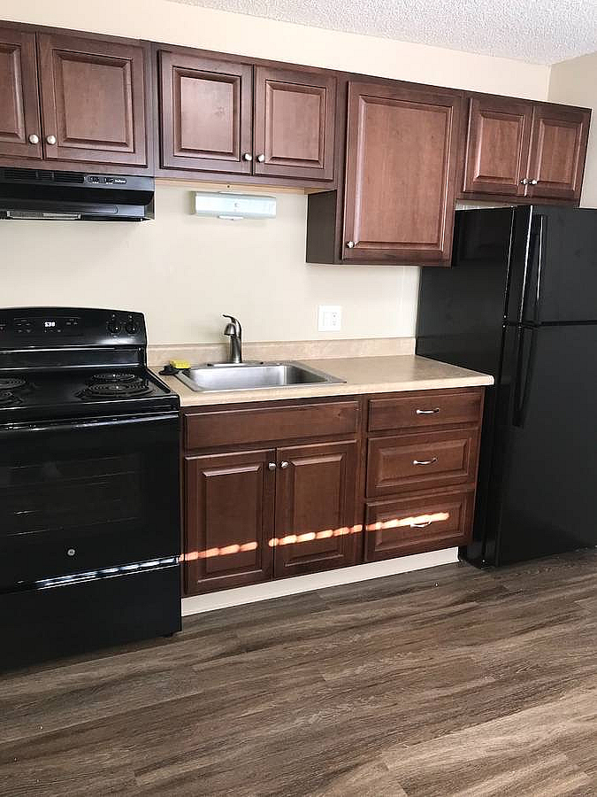 Modern kitchen with dark wooden cabinets, sleek countertops, and black appliances.
