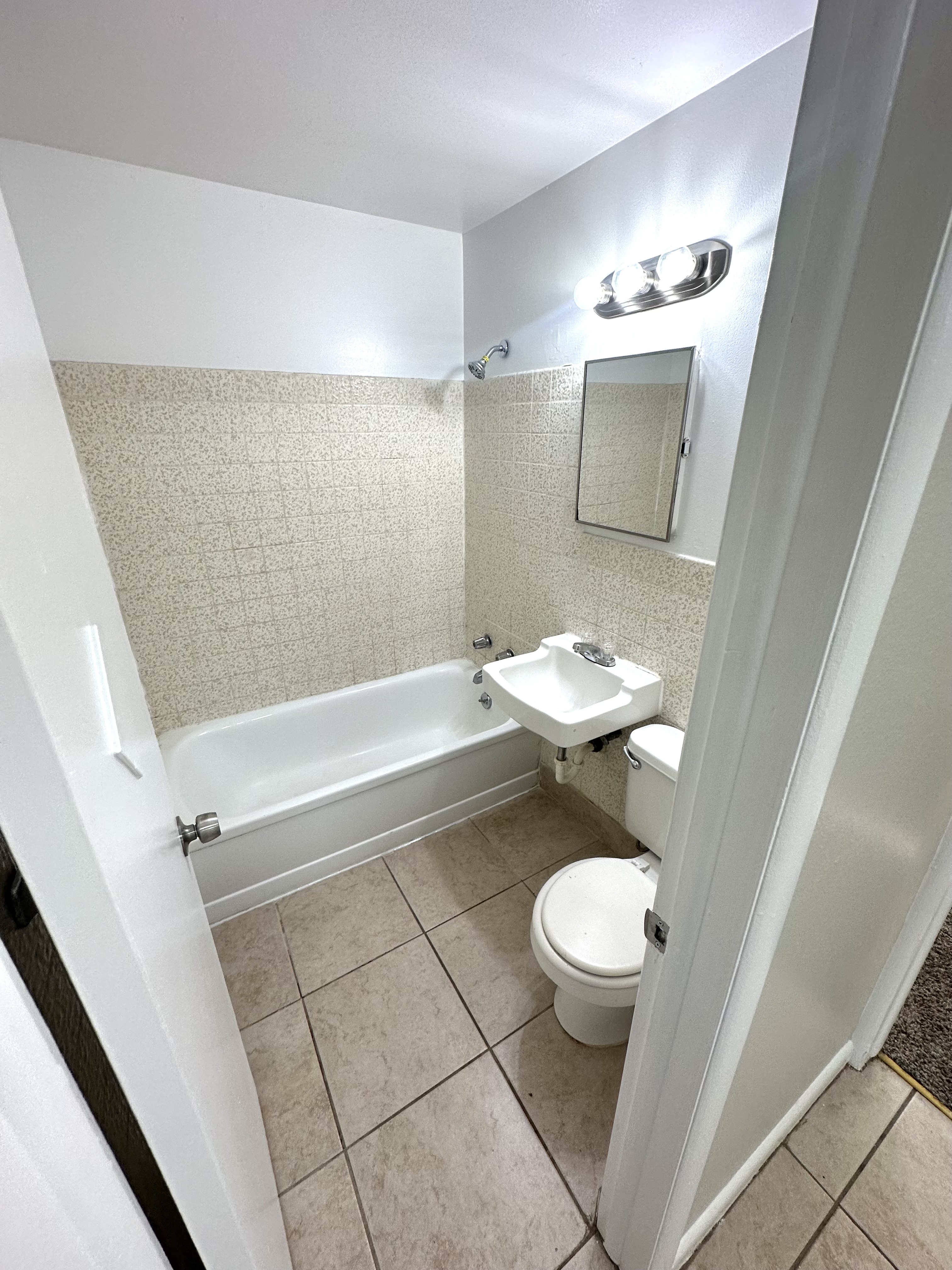 Modern bathroom with gleaming white fixtures, a sleek bathtub, overhead lighting, and elegant tile flooring.