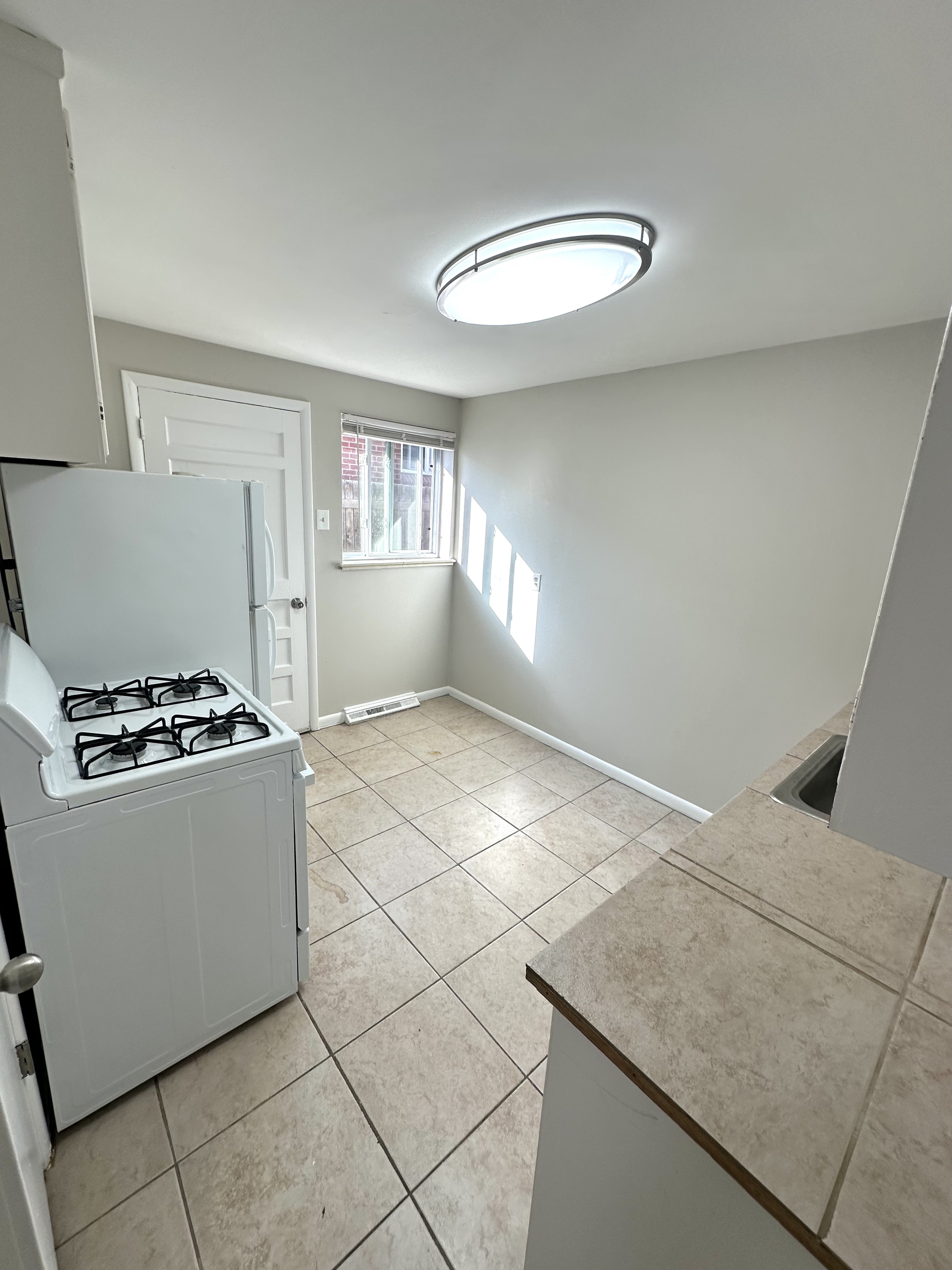 Bright kitchen with large tiles, modern light fixture, and natural light flowing through a window, creating an inviting cooking space.