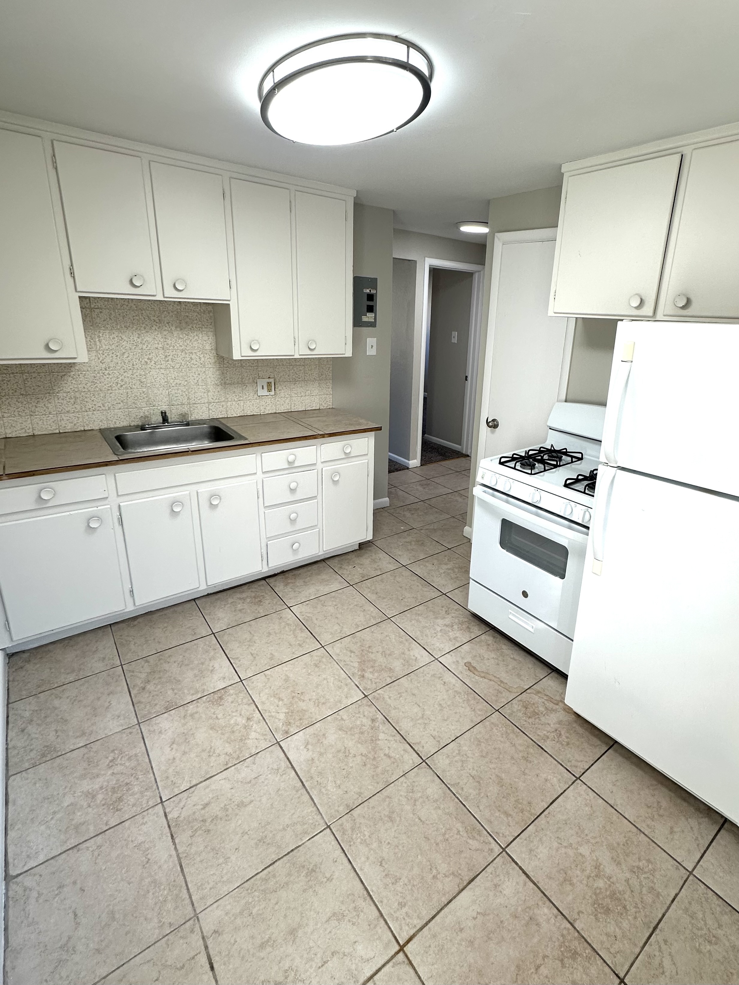Bright and spacious kitchen with modern white cabinetry, tile flooring, and sleek appliances, perfect for culinary creativity.