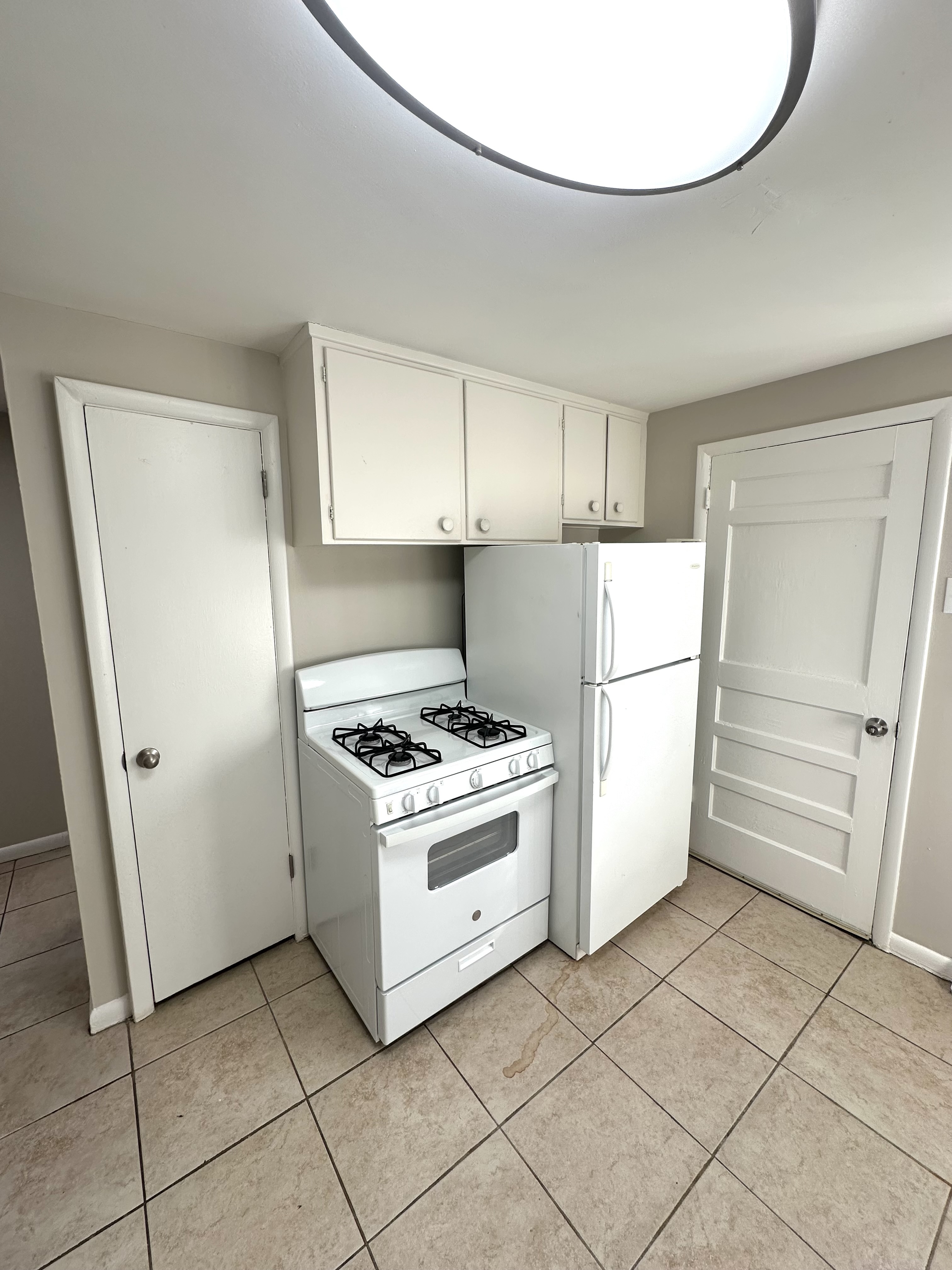 Bright kitchen with modern appliances, featuring a sleek white stove, refrigerator, and ample cabinet space on elegant tiled flooring.